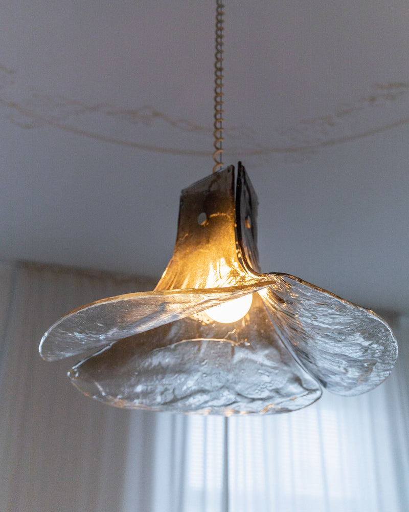 The Carlo Nason "LS 185" Ceiling Lamp from the 1960s by Bottega Jacobs, featuring a metal, flower-shaped shade, hangs from the ceiling, evoking a warm glow reminiscent of Carlo Nason's designs for AV Mazzega. The textured petals lend a rustic, artistic appearance against the smooth, light-colored ceiling.