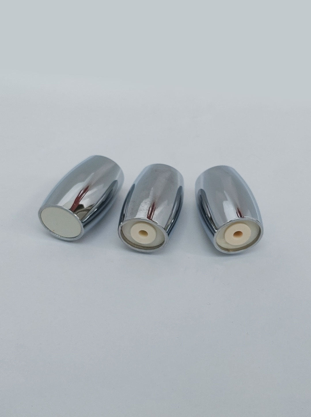 Three silver metal pieces are placed on a light surface, each cylindrical in shape and open at one end. The open ends reveal a beige inner part, likely indicating that these stainless steel items are the Salt & Pepper Set by Les Objoies.