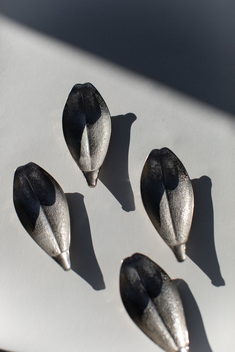 Four metallic leaf-shaped serveware pieces with black and silver finish