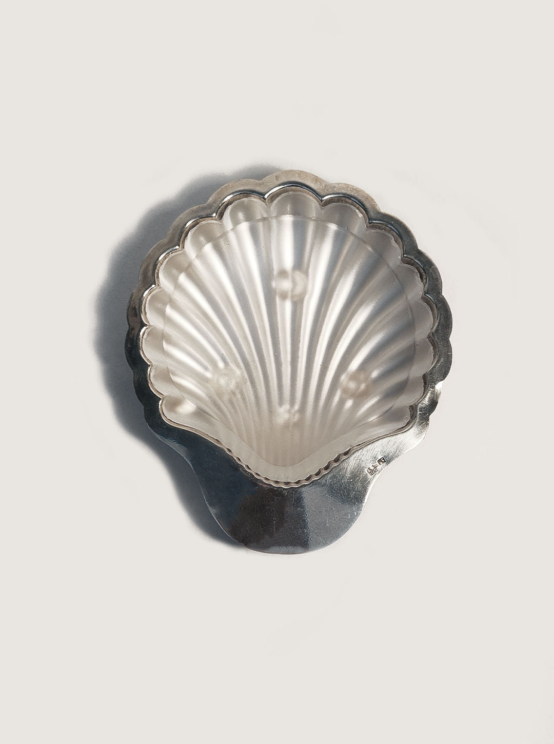 A Shell Butter Dish by Les Objoies, silver-plated with a reflective scallop design, rests on a light background and casts a soft shadow, enhancing any table setting's elegance.