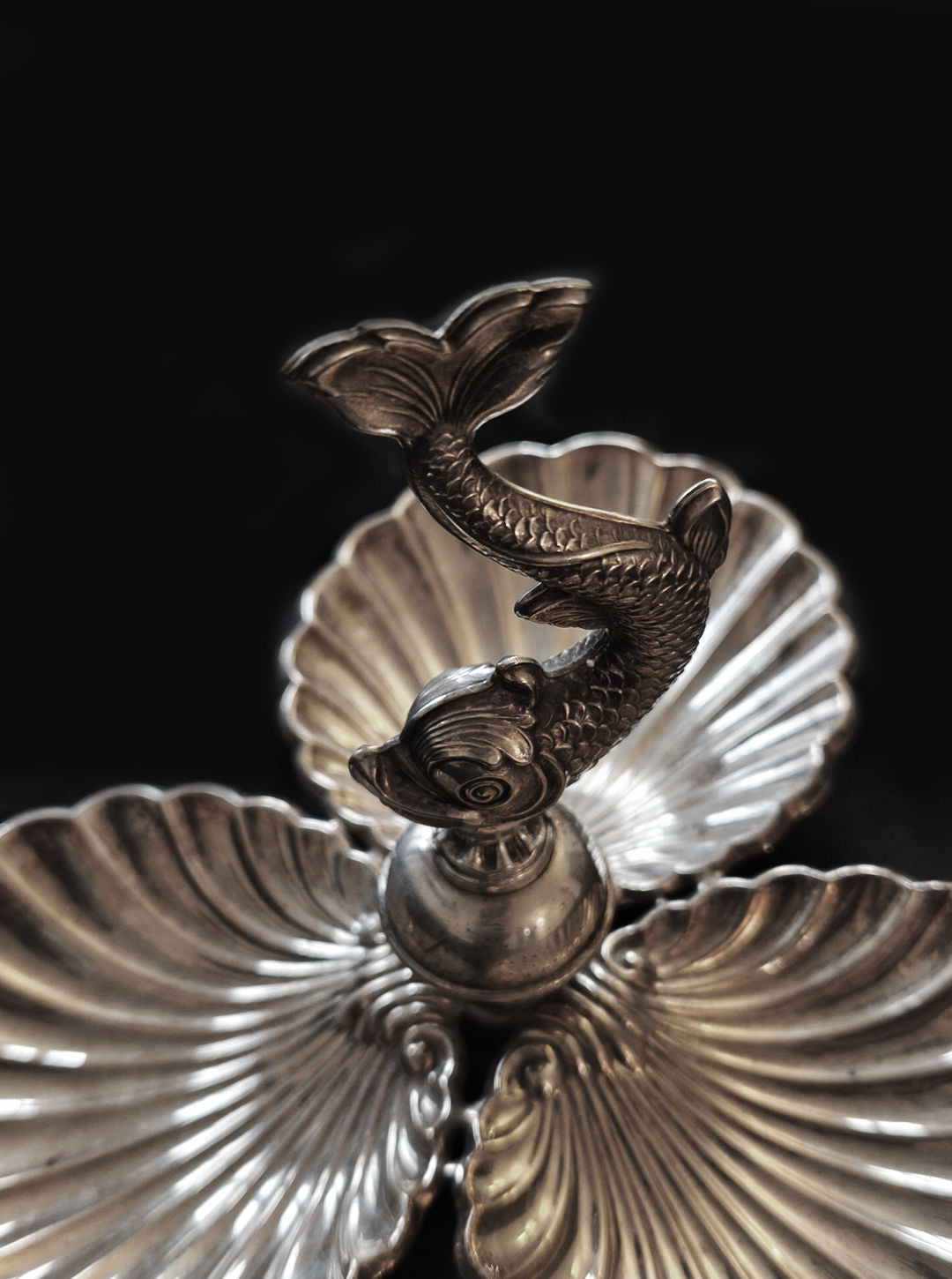 The Shell & Fish Triple Tray by Les Objoies, featuring silver-plated shell-shaped compartments and an ornate dolphin handle, graces the black background.