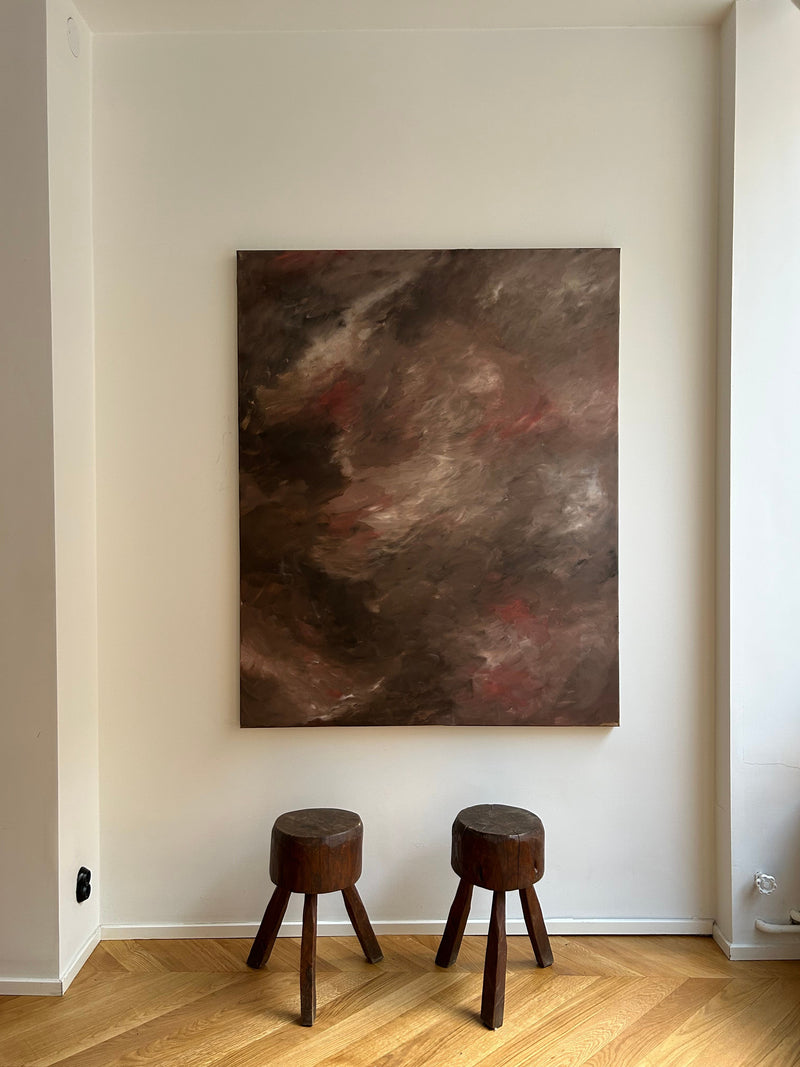 Abstract painting with swirling earth tones displayed above wooden stools