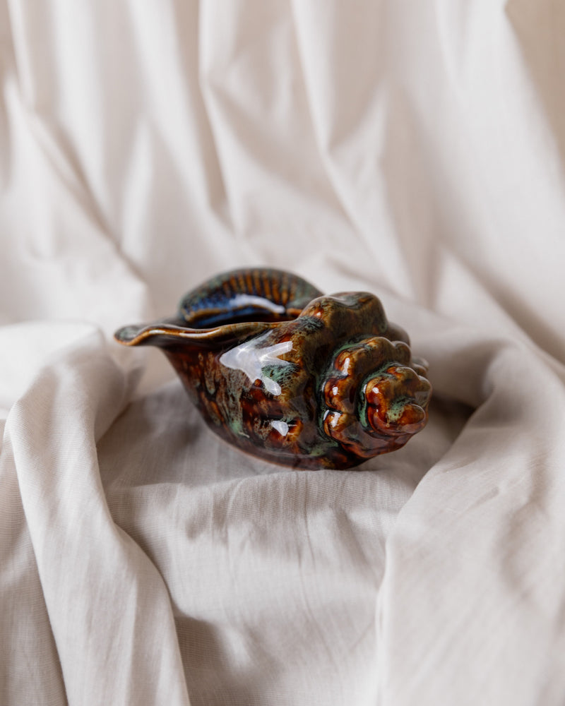 The Studio Keramik Italy 70s Ceramic Bowl by Bottega Jacobs, with its vintage seashell shape and glossy multicolored finish, rests on white fabric. Its intricate design mimics natural shell patterns, creating a striking decorative element in any setting.