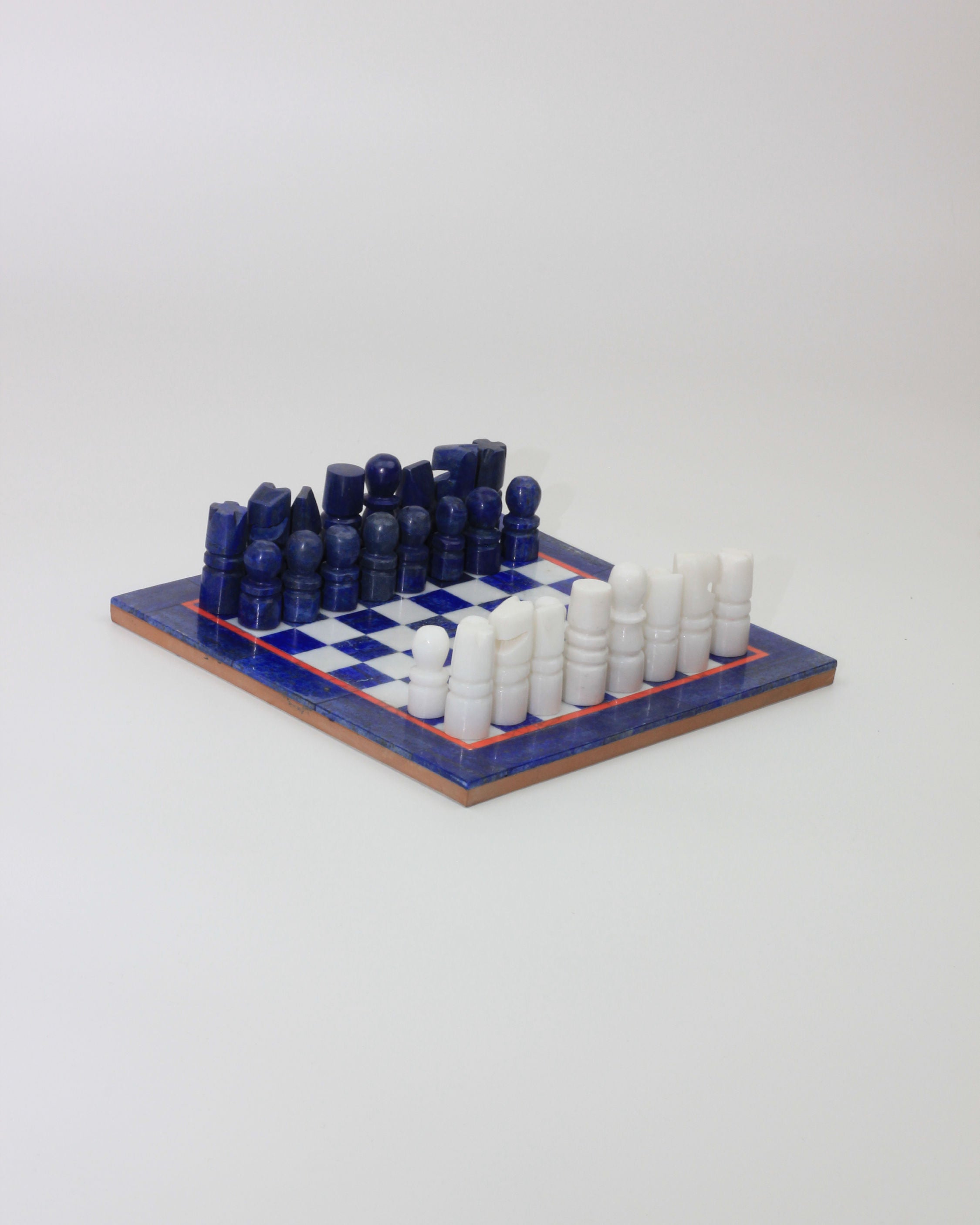 A compact, square Lapis Lazuli Chessboard from Boga Avante Shop features a striking blue and white checkered pattern. The chess pieces, divided into blue and white sets, are neatly arranged in their starting positions. This vintage chess set exudes charm against a simple white background.