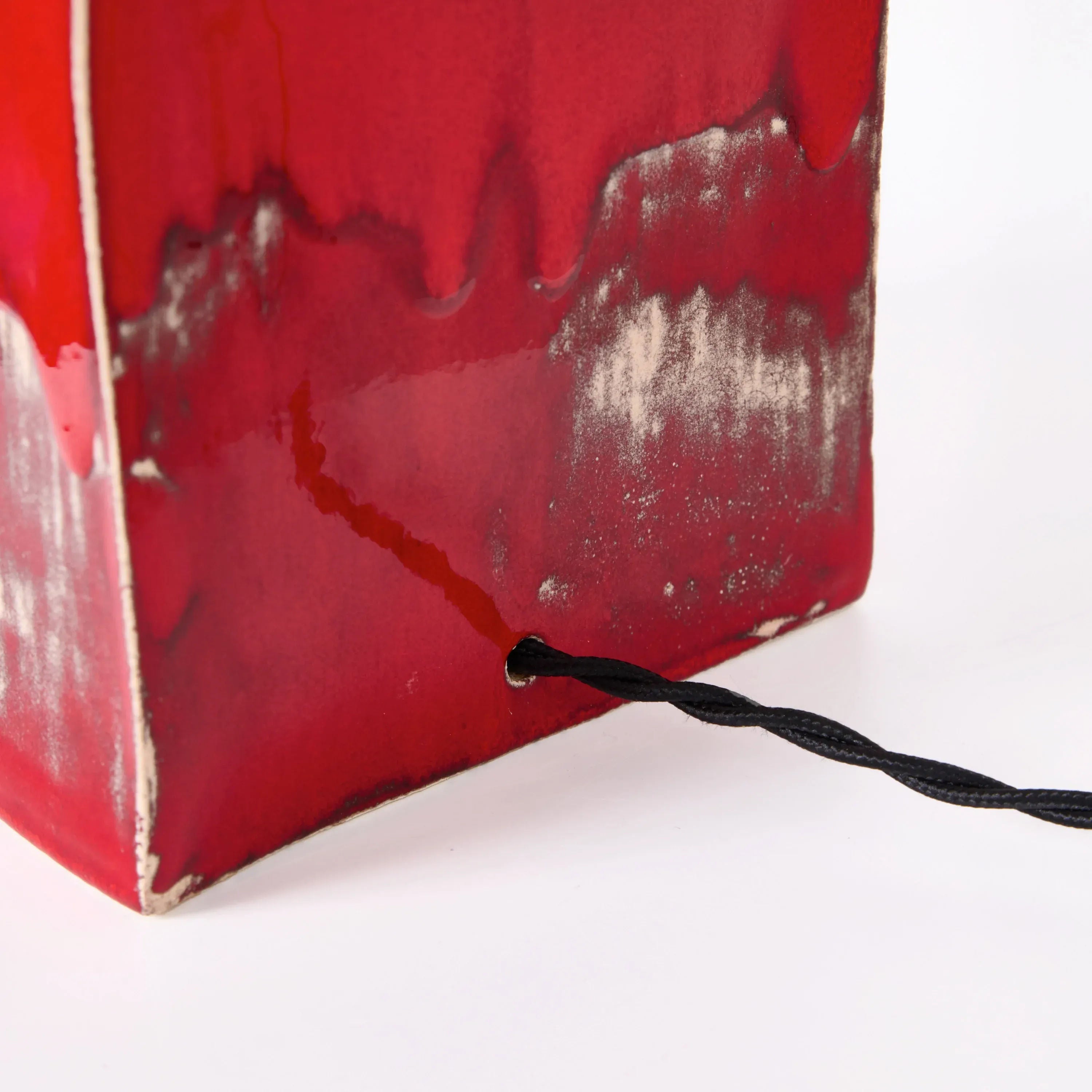 A close-up of the Arouca Table Light Red by Project 213A shows its glossy ceramic base with a black twisted cord emerging from the corner, set against a white background.