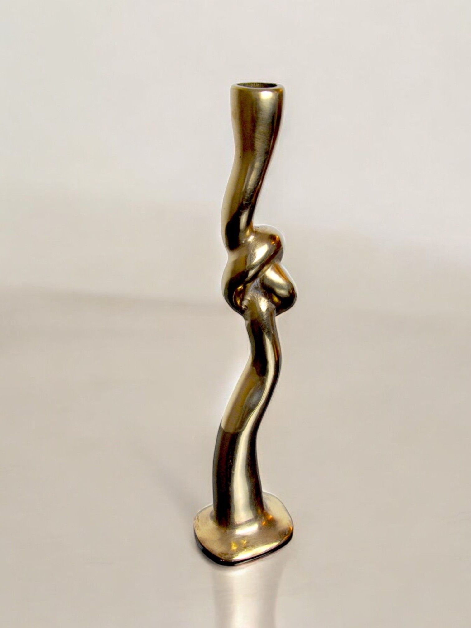 The Brutalist Knot Candleholder in Bronze 70s by Malamar Studio is a tall, abstract piece featuring a twisted, flowing design that exudes Italian elegance, resembling an elongated figure with curves set against a plain background.