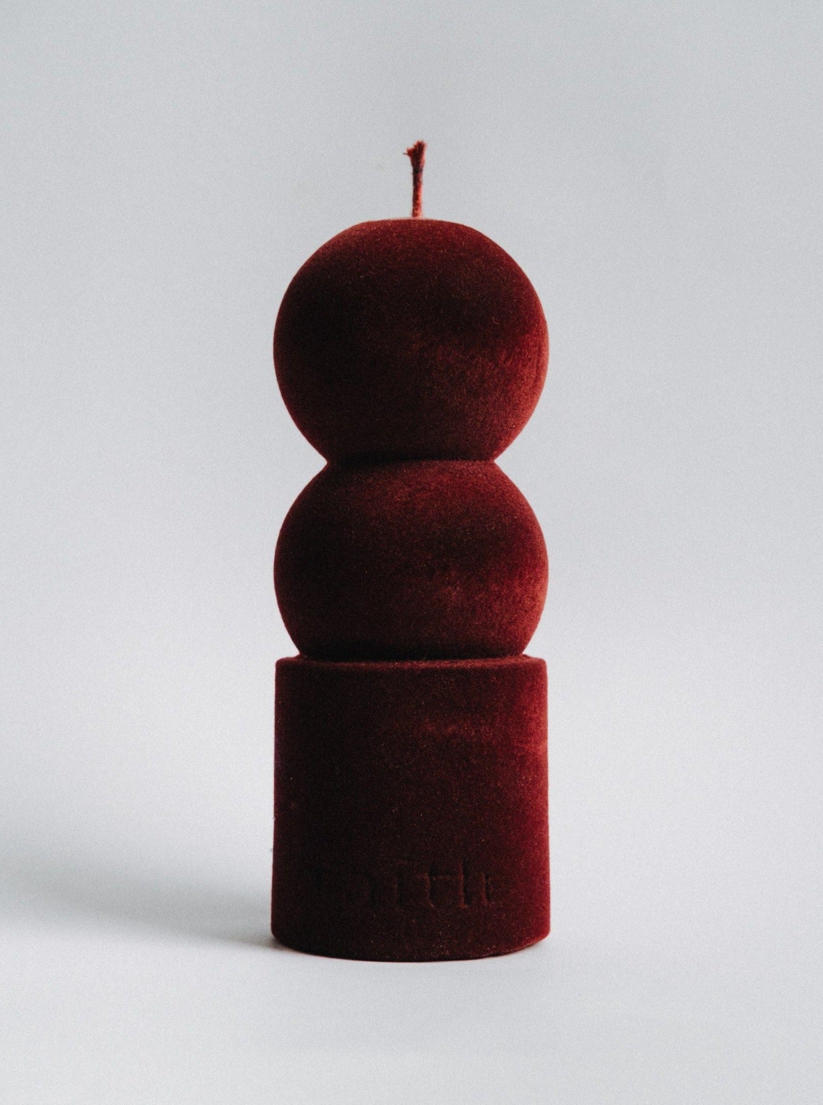 A velvety red **Lilu Candle Wine Velvet Edition** by **Taith** with a unique design featuring two spherical sections stacked on a cylindrical base, set against a plain white background. Crafted from natural soy wax, the candle wick protrudes from the top of the upper sphere, creating an eco-conscious ambiance.