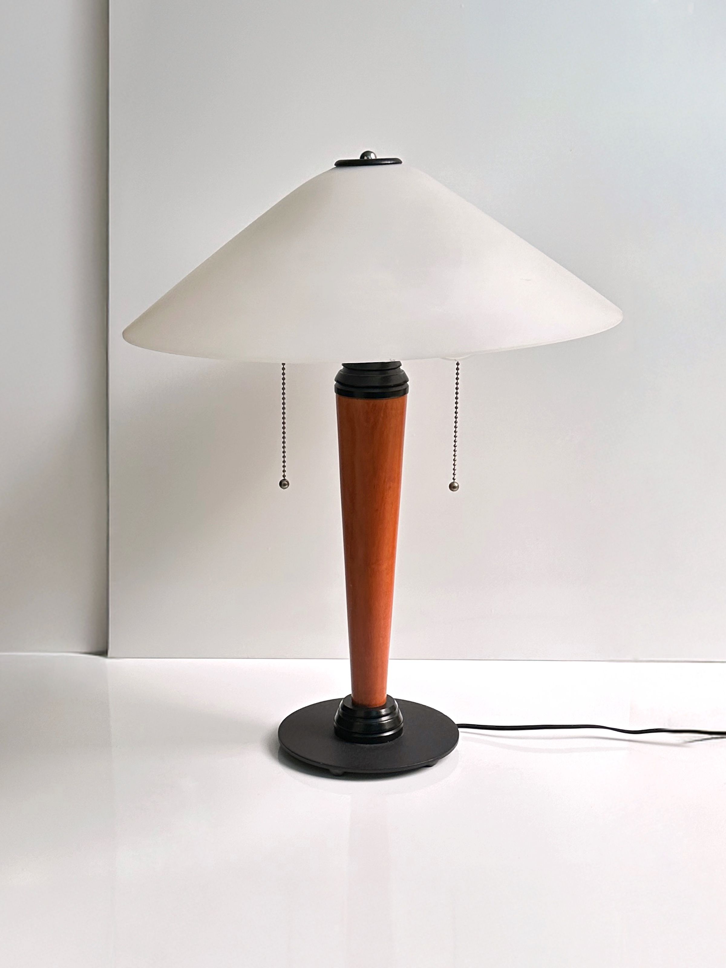 The 1950s Scandinavian Banker Lamp by Dodo Vintage is a sleek table lamp featuring a white conical shade, a wooden tapered base, and a black lacquered metal round bottom. It includes two pull chains for operation and is displayed against a plain white background.