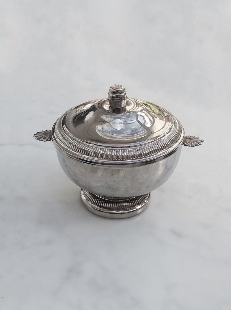 A white ceramic sugar bowl with a lid and spoon on a kitchen countertop