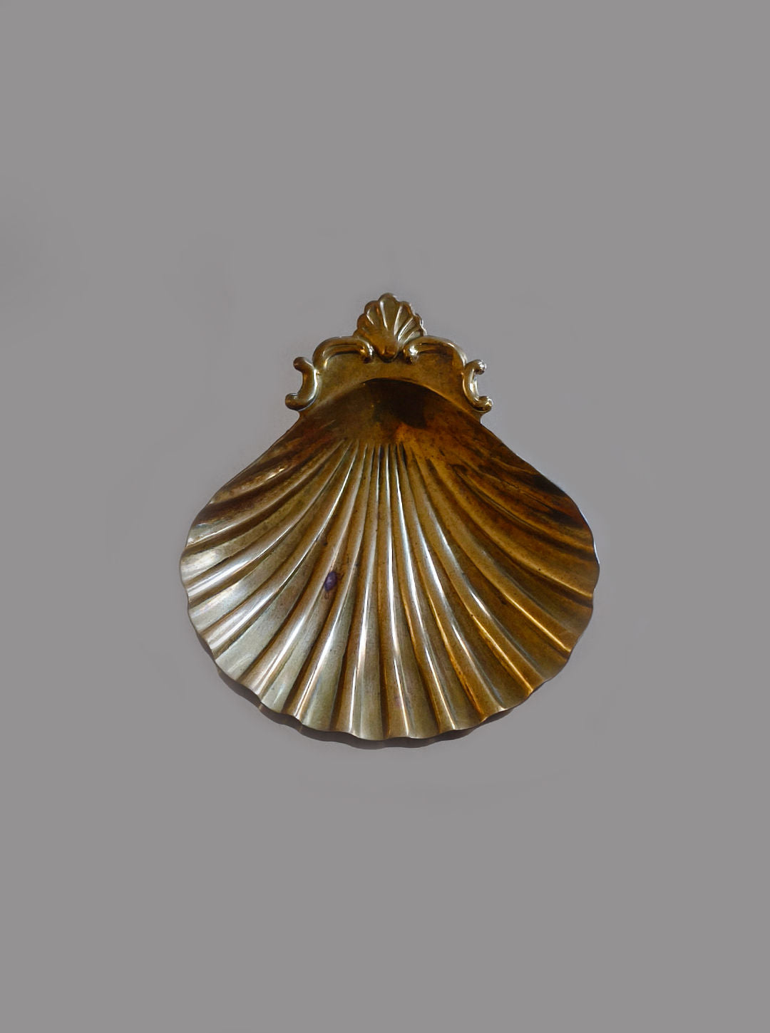 The Shell Brass Vide Poche by Les Objoies features ornate detailing and a shiny, reflective surface. Its seashell shape and ridged design add sophistication while offering an elegant spot for small items, all set against a plain gray background.