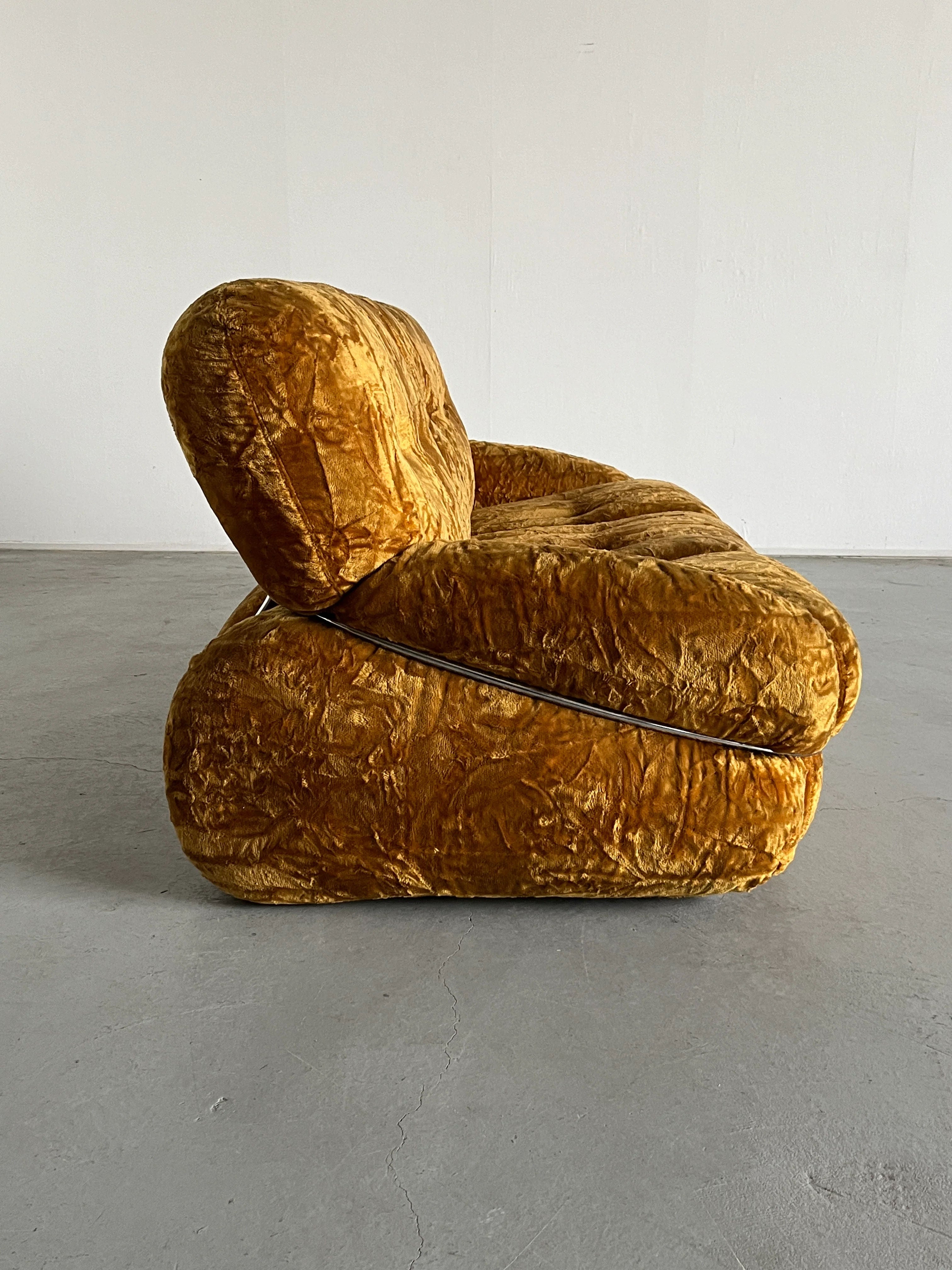 Side view of the plush ochre velvet 'Okay' Sofa by Cherry Cargo. Its thick cushions and Mid-Century silhouette grace a polished concrete floor against a plain white wall, highlighting its iconic 1970s design.