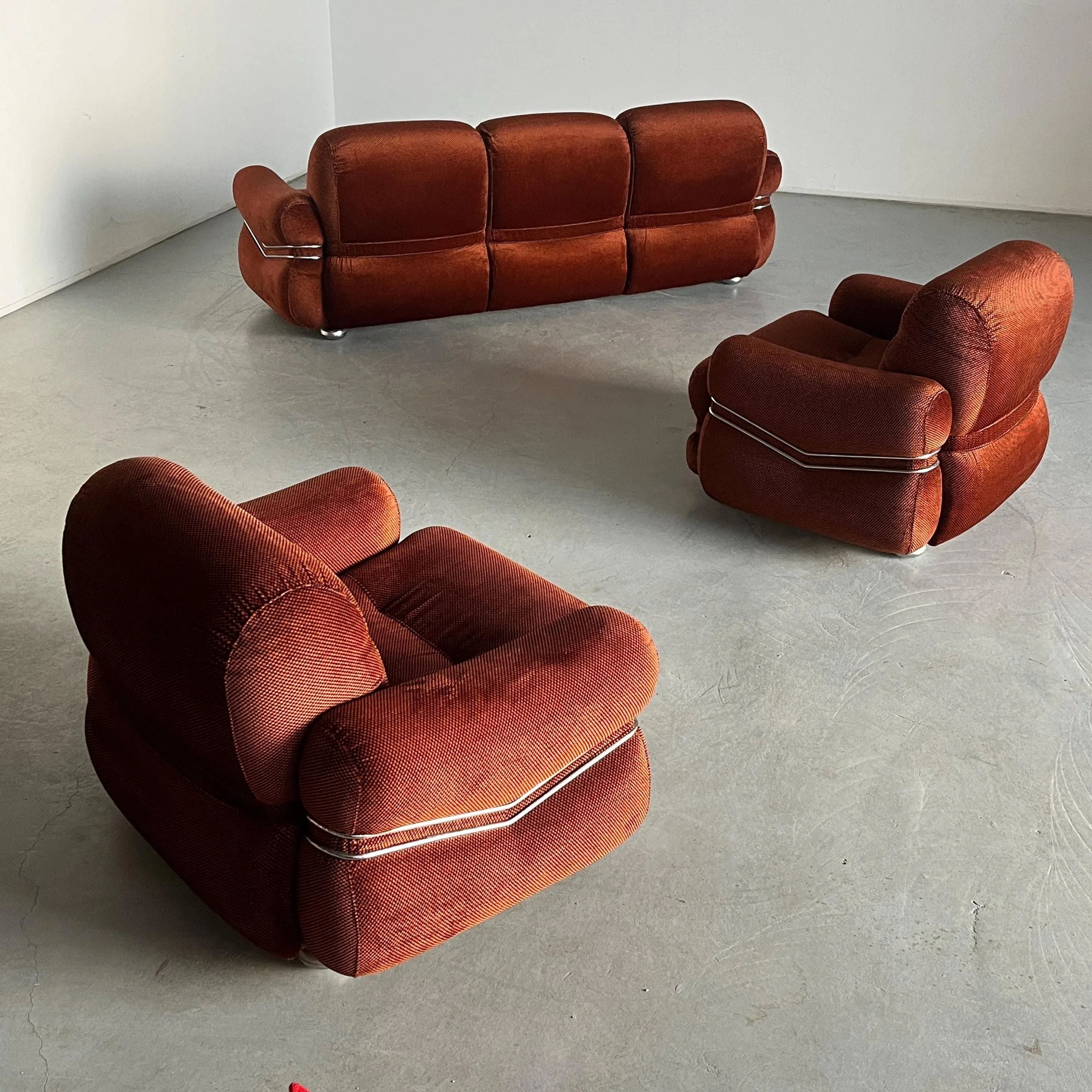 The Italian Space Age Seating Set by Cherry Cargo, featuring checkered upholstery from the 1970s, is arranged on a smooth concrete floor in a minimalist space with white walls. The set's rounded cushions and silver accents evoke a retro style.