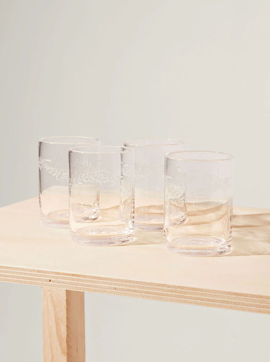 Four Akua Objects Barbro Water Glass Large tumblers with delicate floral patterns, positioned closely together on a wooden table against a neutral background.