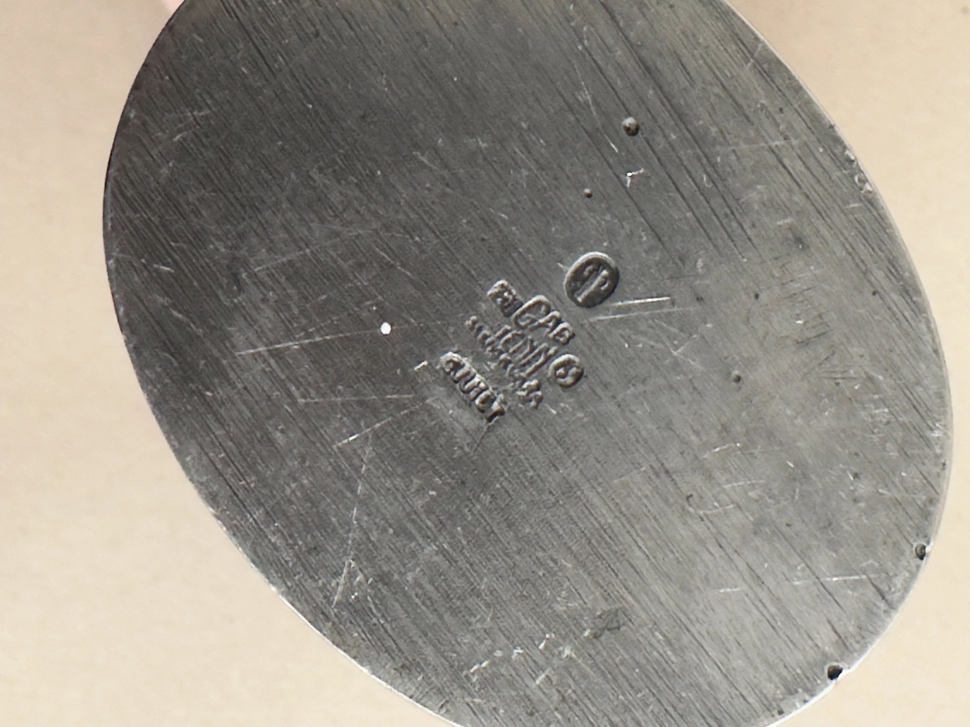 A close-up of a cast pewter object from Galerie Storm resembles an Art Deco vase design. Engravings include "ACP," "9201D," a copyright symbol, and "CHINA." The metal's surface displays scuffs and scratches.