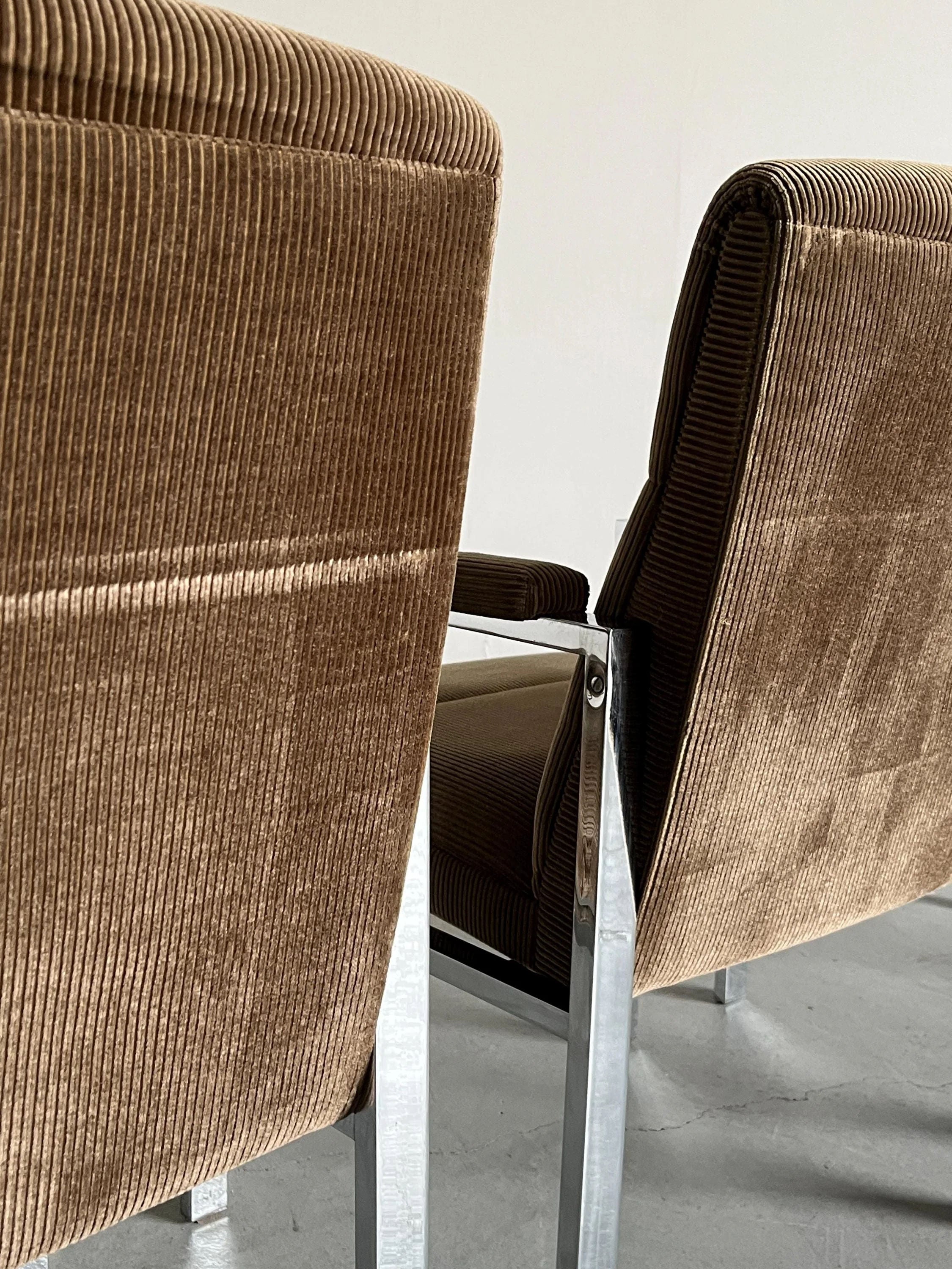 Close-up of Cherry Cargo's Mid-Century Armchairs, 1970s, featuring brown corduroy upholstery and chromed steel frames on a light gray floor. The chairs face a neutral wall, emphasizing their textured fabric and sleek metal design.