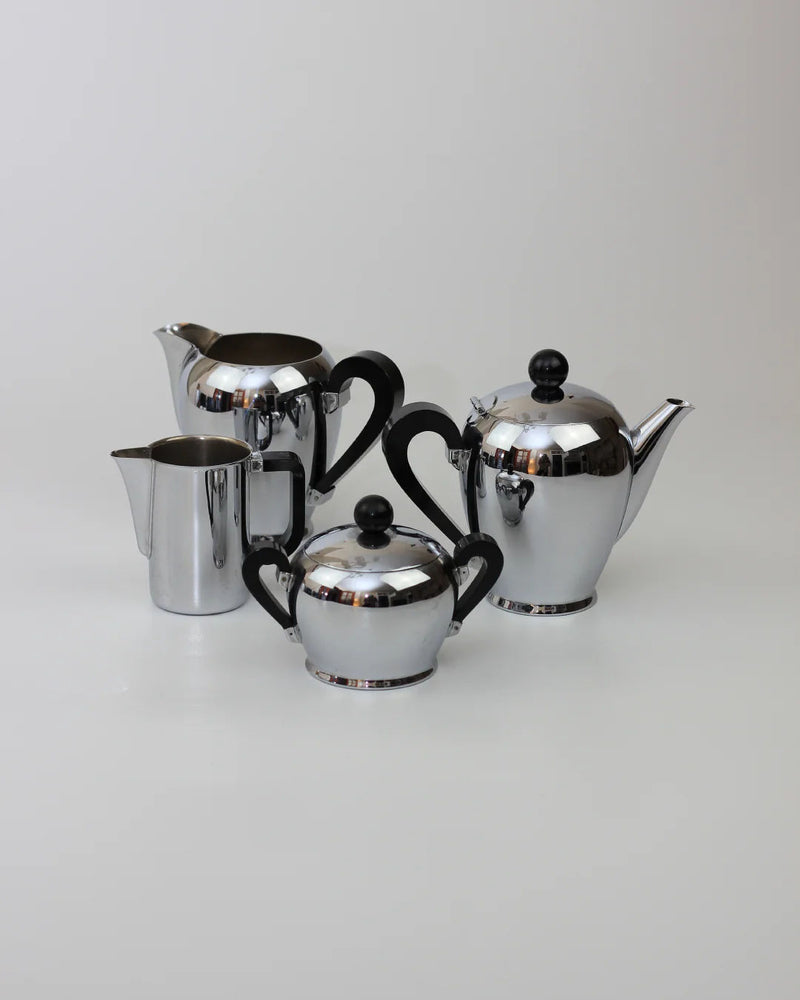 The Boga Avante Shop Italian Coffee and Tea Set, 1945, features four shiny silver pieces—teapot, sugar bowl, creamer, and coffee pot with black handles—exemplifying mid-century Italian elegance on a neutral background.