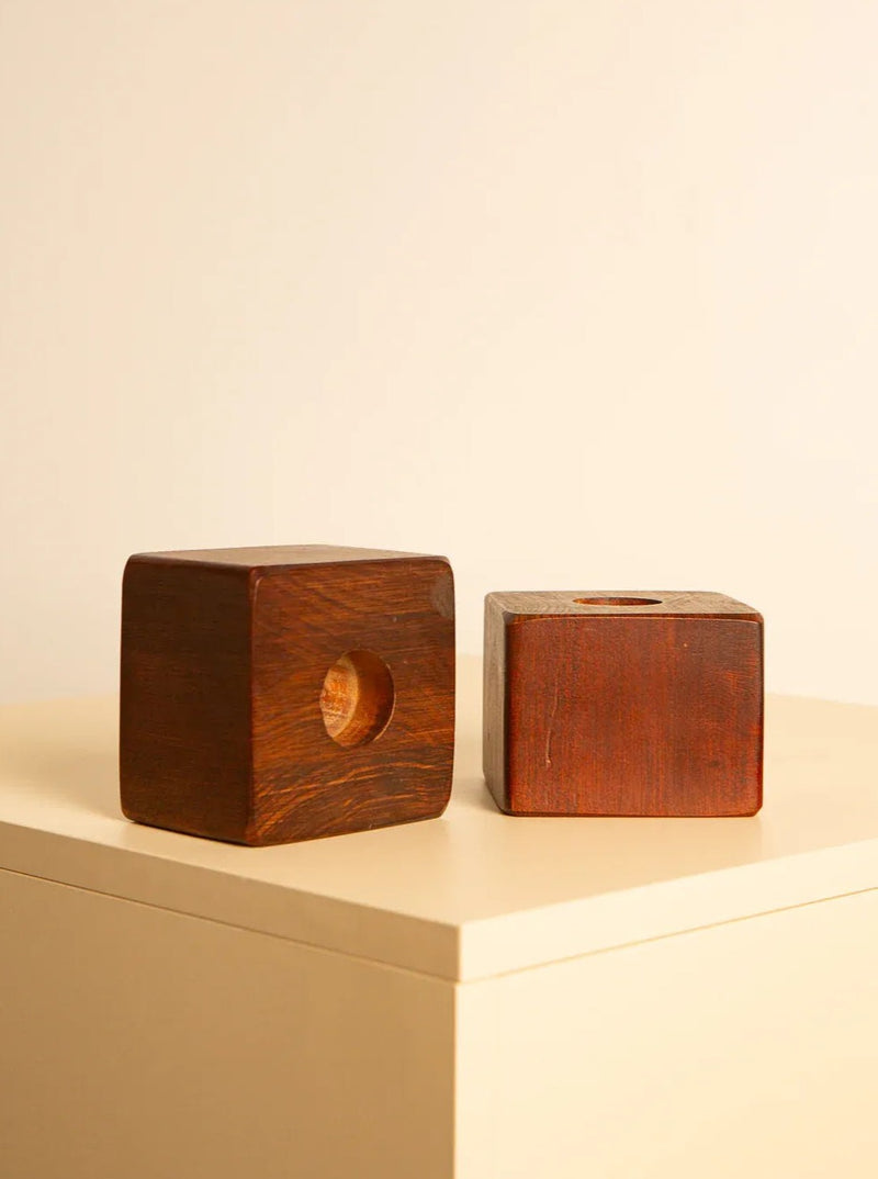 Two vintage Pair of Cube-Shaped Wooden Candleholders 80's by Treaptyque with differently shaped holes rest on a light beige surface. One cube has a round hole, while the other has a square hole. The cubes boast Italian craftsmanship, showcasing a rustic, polished finish against a light background.