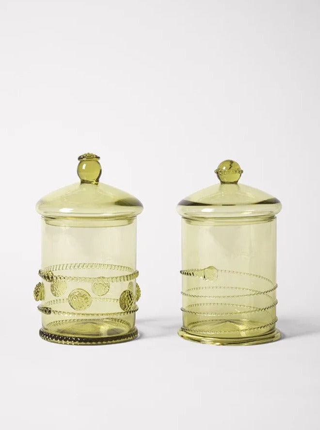 Two vintage-style translucent green glass jars with lids are shown. Crafted as exquisite handmade bonbonnières, one jar has a decorated knob and a series of embossed designs spiraling around the body, while the other features a simpler knob and smoother spiral decorations reminiscent of Akua Objects' Karl Bonbonnière Swirl.