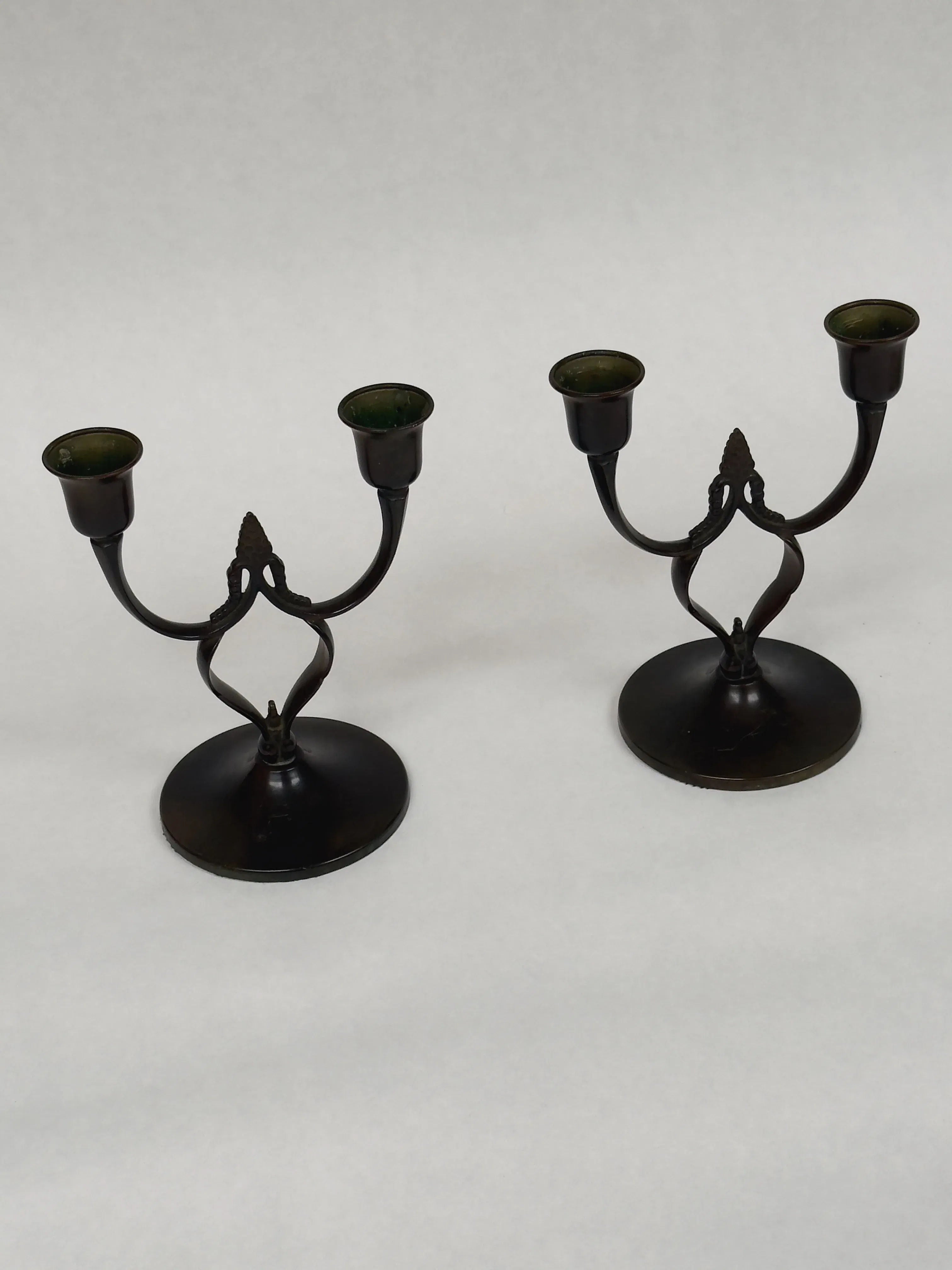 A Pair of Antique Bronze Candlesticks by Galerie Storm, featuring Art Nouveau style with two holders each, elegantly curved arms, and circular bases against a plain white backdrop.