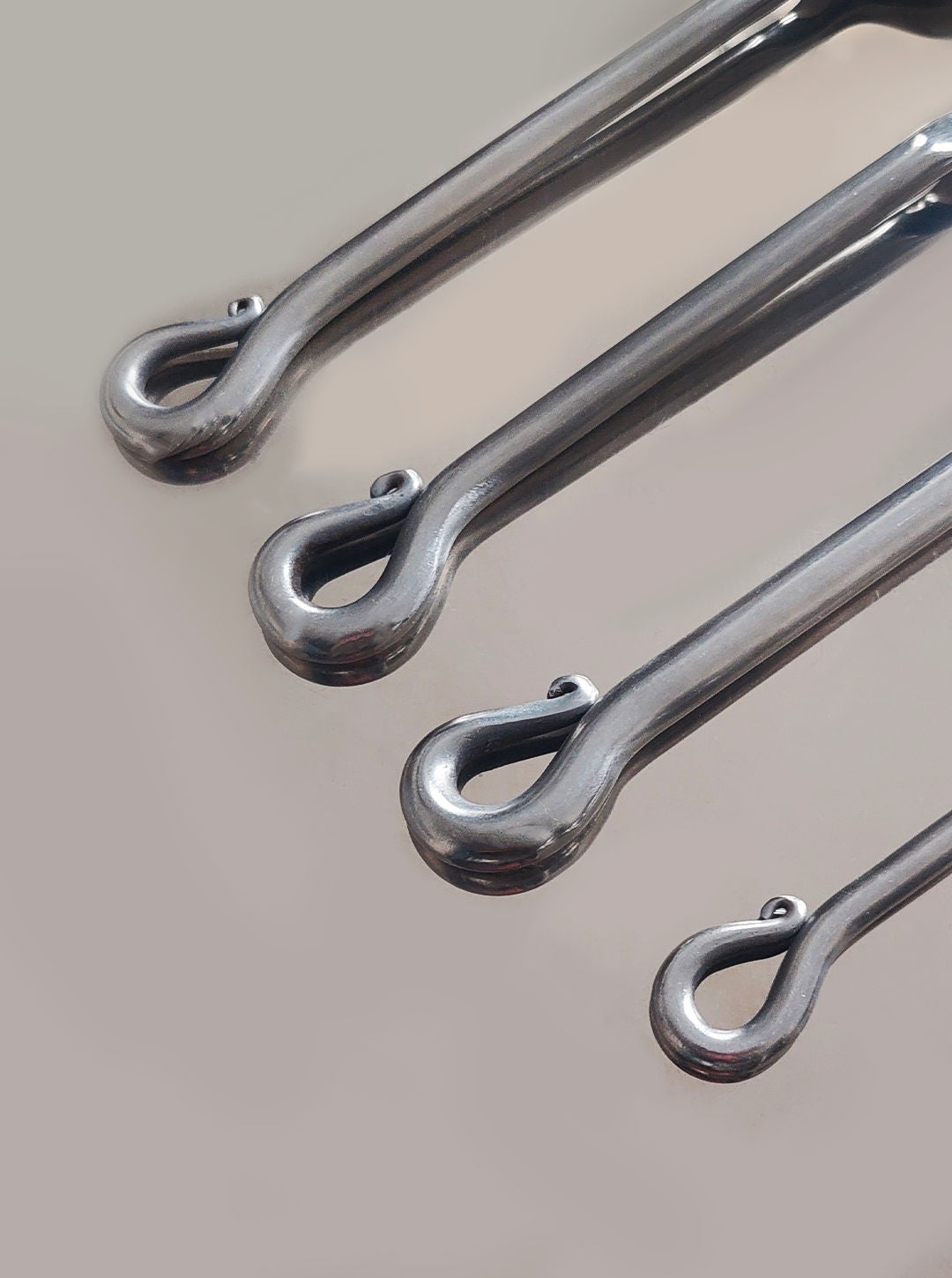 A photo showcasing the Les Objoies "Vintage Set of 4 Twist Cutlery," featuring four pieces of stainless steel flatware with elegantly looped handles, neatly arranged in descending size order from top to bottom on a smooth, light-colored surface—evoking the presentation of timeless vintage cutlery.