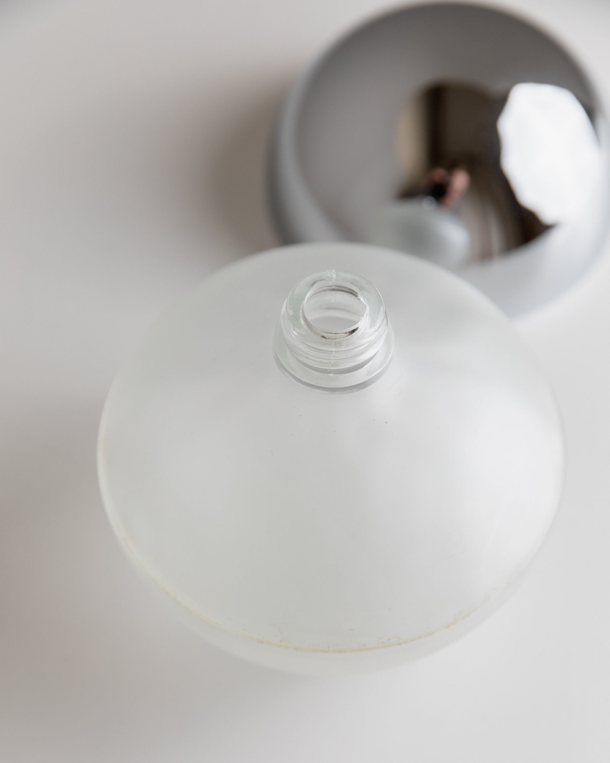 A frosted vintage Bottega Jacobs Liqueur Bottle from Italy, 1980s, with a narrow neck and metallic cap rests open on a white surface. The cap's reflective chrome hints at light and color, subtly echoing a space-age design while casting soft shadows.