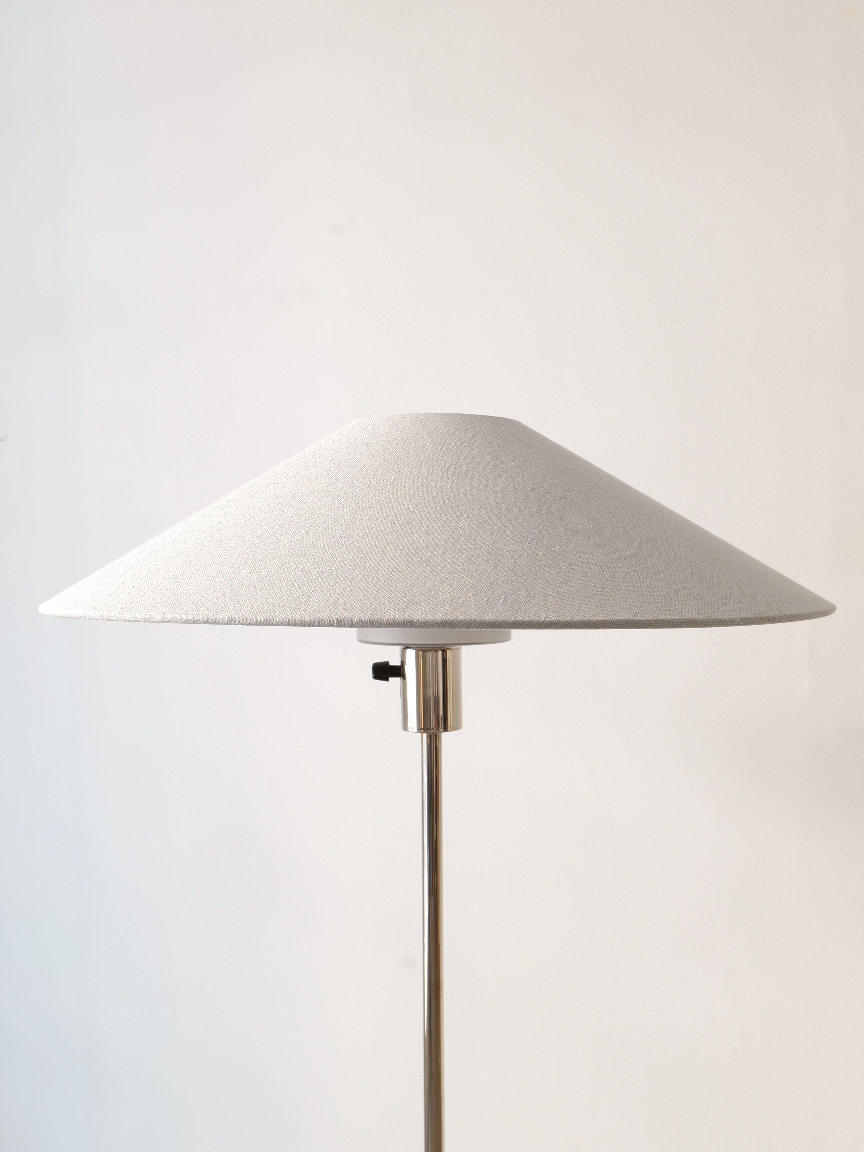 A Deco Floor Lamp Harald Notini 1940s with a conical white fabric shade and a sleek, slender metallic stand embodies Swedish Modern design. Reminiscent of Harald Notini's timeless creations from Arvid Böhlmarks Lamp Factory, it stands elegantly against a plain white background. This beautiful piece is featured in the Collection apart brand.