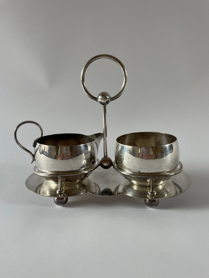 Introducing the Maud Vaughan Antique Silver Plate Tea Service Set, reminiscent of vintage UK c. 1910 designs. This refined set includes a gracefully spouted creamer and a matching bowl, both elegantly displayed on a smooth, reflective tray with a handle.