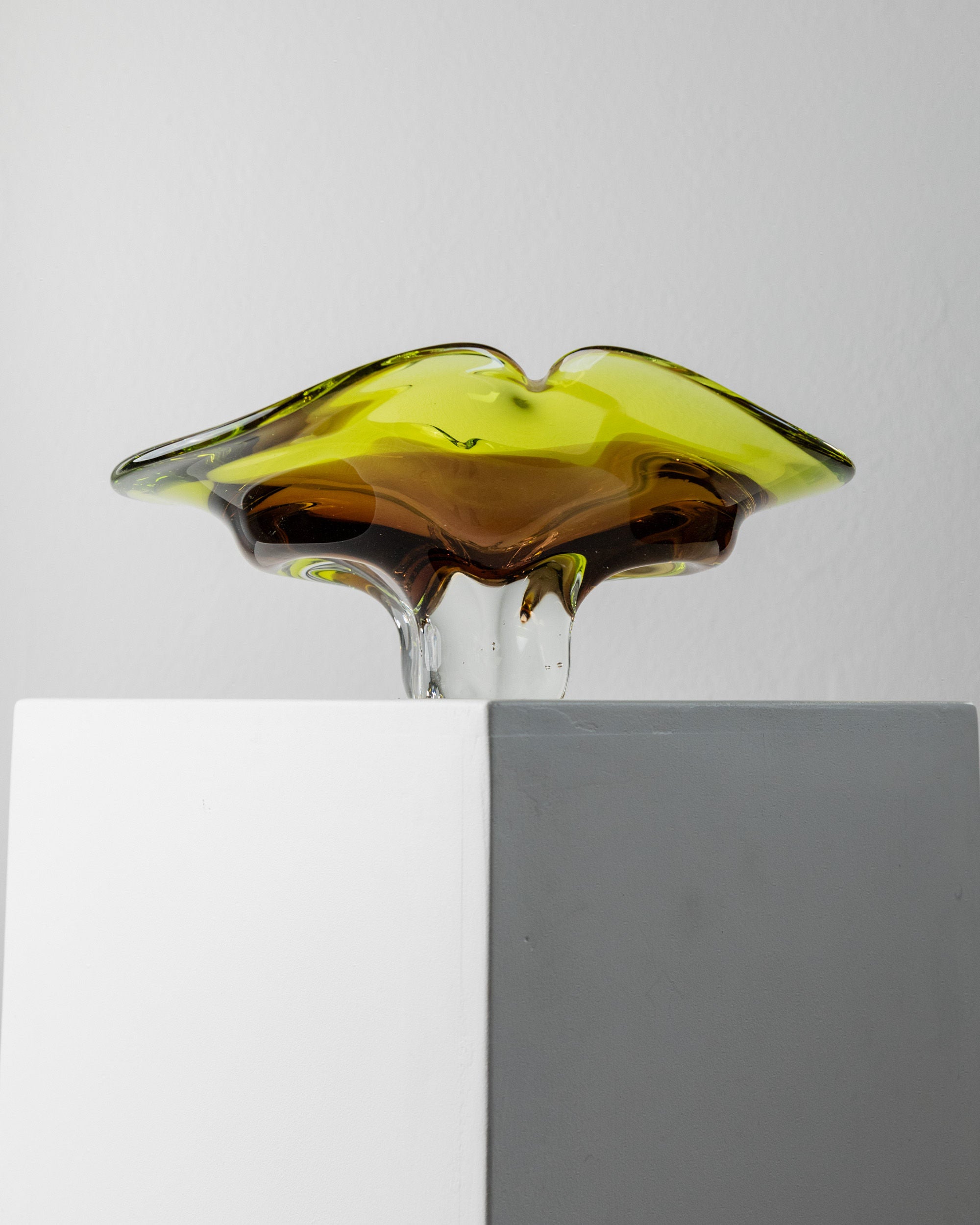 The Murano Glass Bowl by Bottega Jacobs, crafted in Italy during the 1970s, features a flowing abstract design in green and amber tones. Its mid-century aesthetic stands out beautifully against a minimalist backdrop.