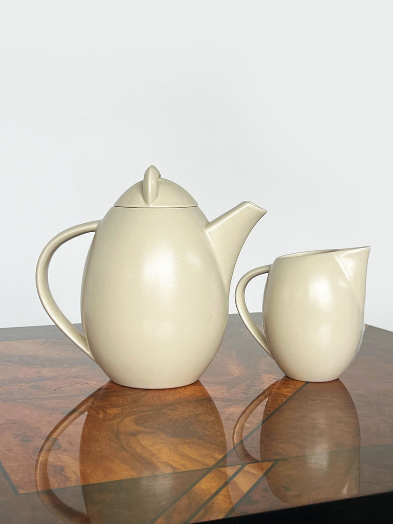 Cream ceramic teapot and milk jug set on polished wood surface