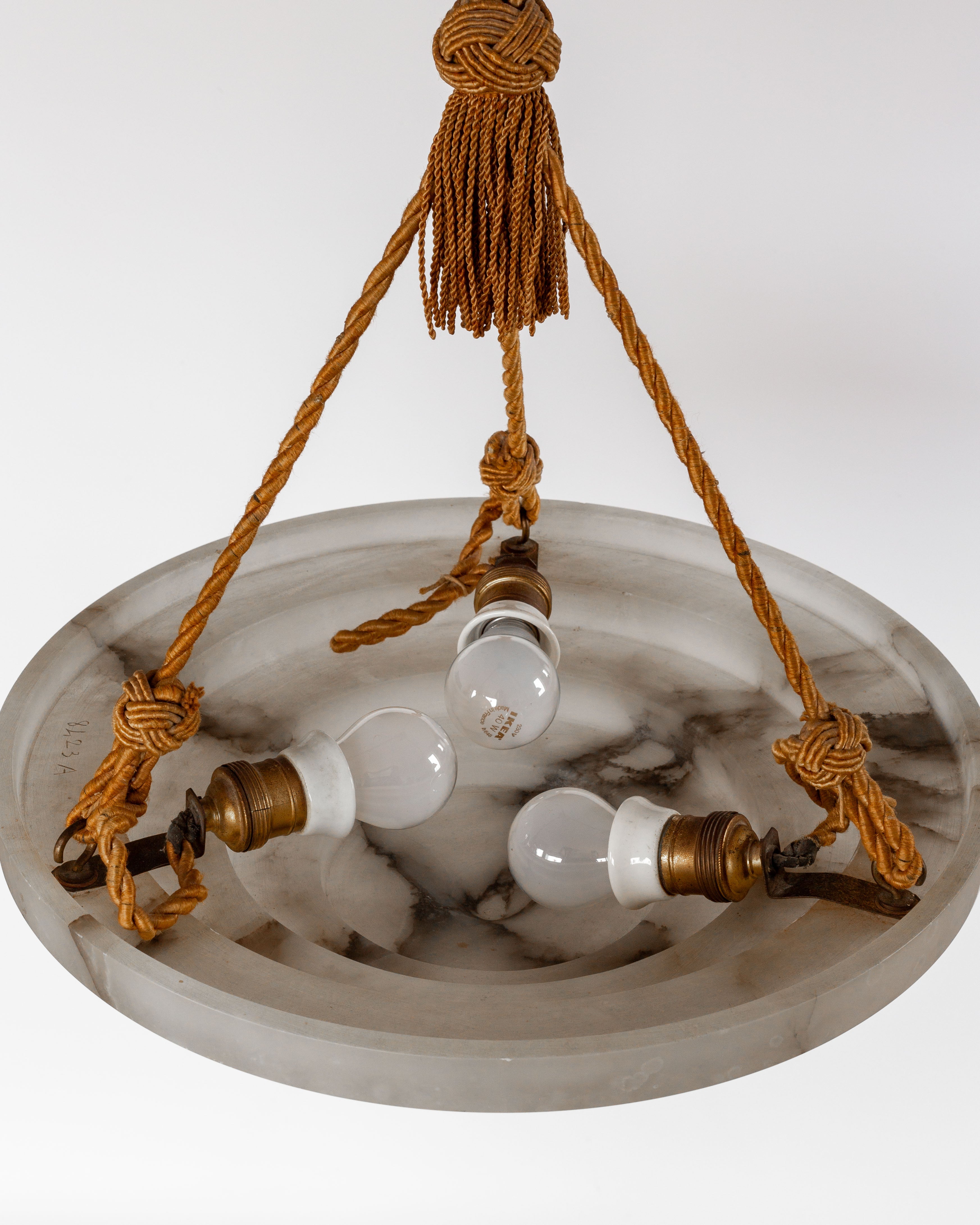 The Spigel Art Deco Alabaster Pendant Chandelier features a marbled glass shade with three bulbs connected by brown twisted ropes and brass fittings, ending in a decorative knot. Its striking alabaster lighting effect contrasts beautifully against the solid white background.