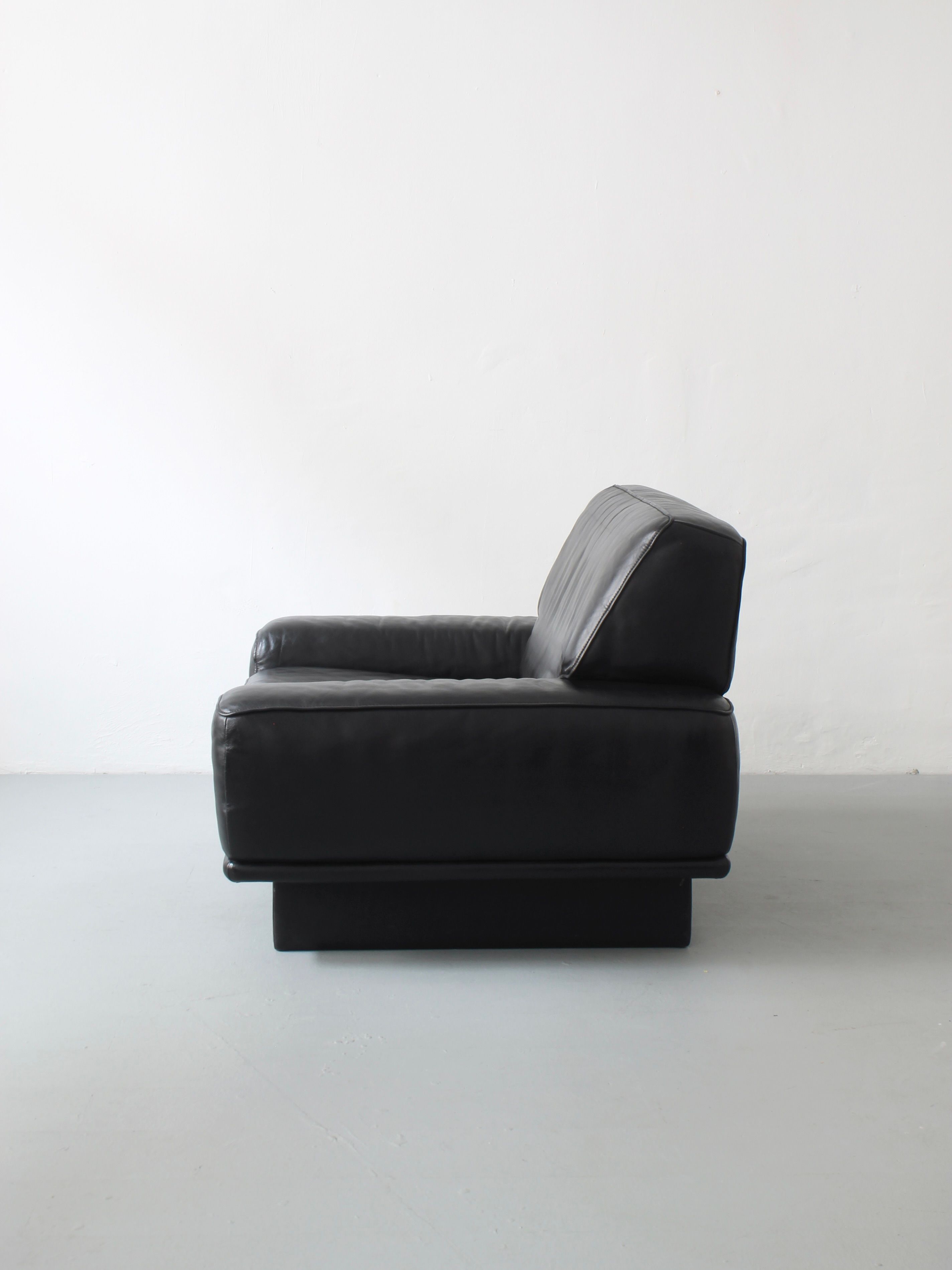 The Lounge Chair by De Sede from Afterhour Furniture boasts a sleek, modern design with square armrests, made from high-quality black leather. Its minimalist style echoes Swiss luxury, beautifully showcased against a plain white background.