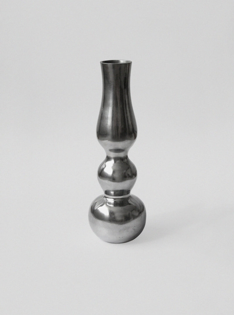 The Aluminum Figure Vase by Vintage Stories features a reflective, sculptural design with a mirror finish. It stands out on a plain light gray background, capturing the essence of minimalist style.