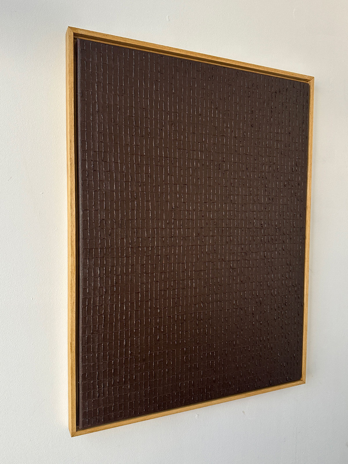 The "Burnt Umber - Oil on Canvas" by Roi Elmaliah is a expertly crafted, textured abstract painting featuring a grid-like pattern in a wooden frame, elegantly displayed on a white wall.