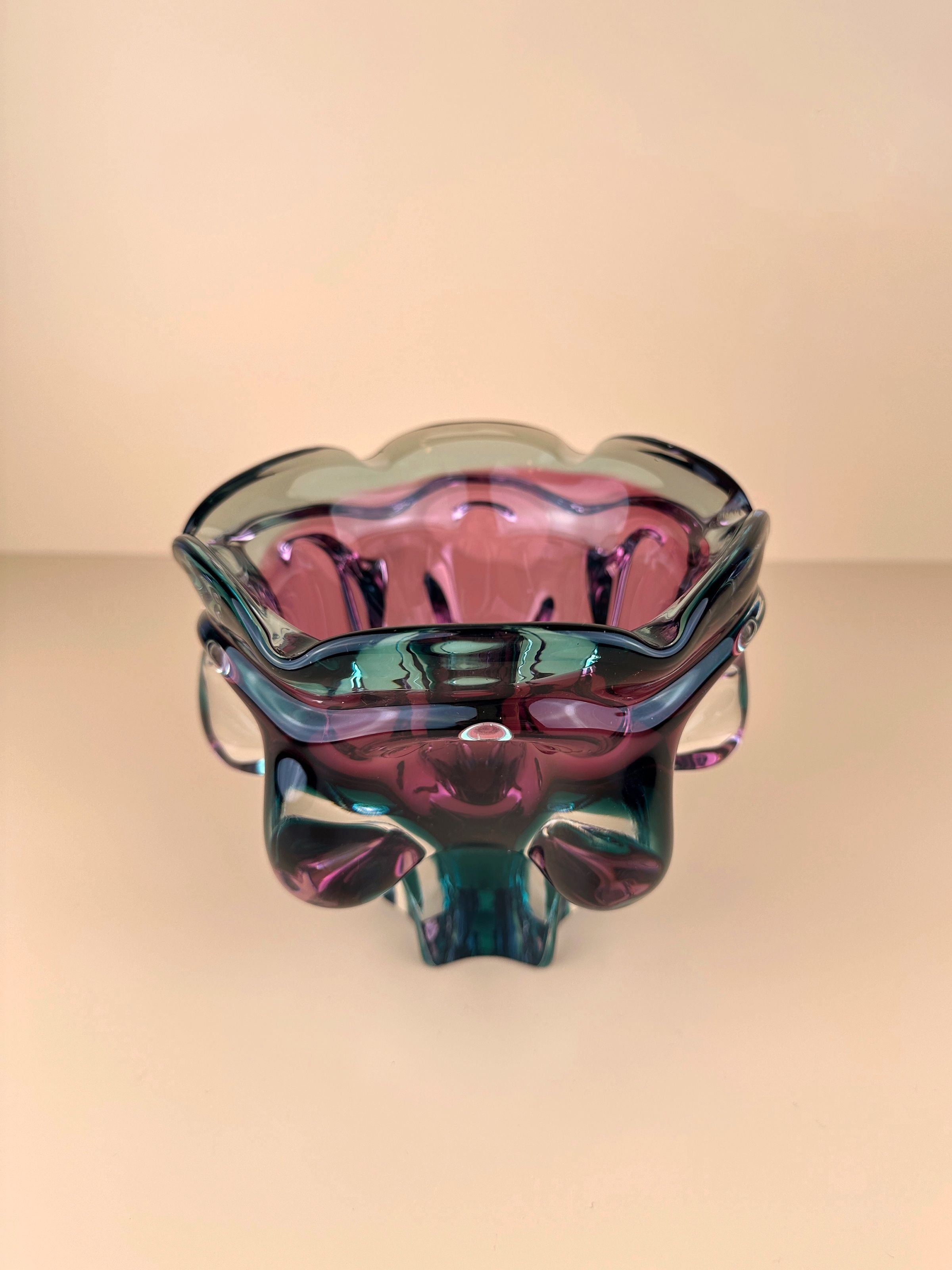 A multicolored, abstract glass bowl with a scalloped rim and wavy edges. This Large Bohemian Bowl in two tone technique by Dodo Vintage, inspired by Chribska glassworks and designed by Josef Hospodka, features blends of pink, green, and hints of blue, creating a striking, translucent art piece set against a neutral background.