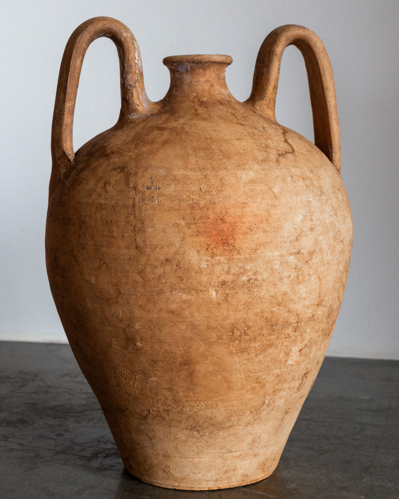 The Spigel Early 20th Century European Ceramic Vase, featuring a rounded body, narrow neck, and two curved handles, rests on a smooth gray surface against a plain light background.