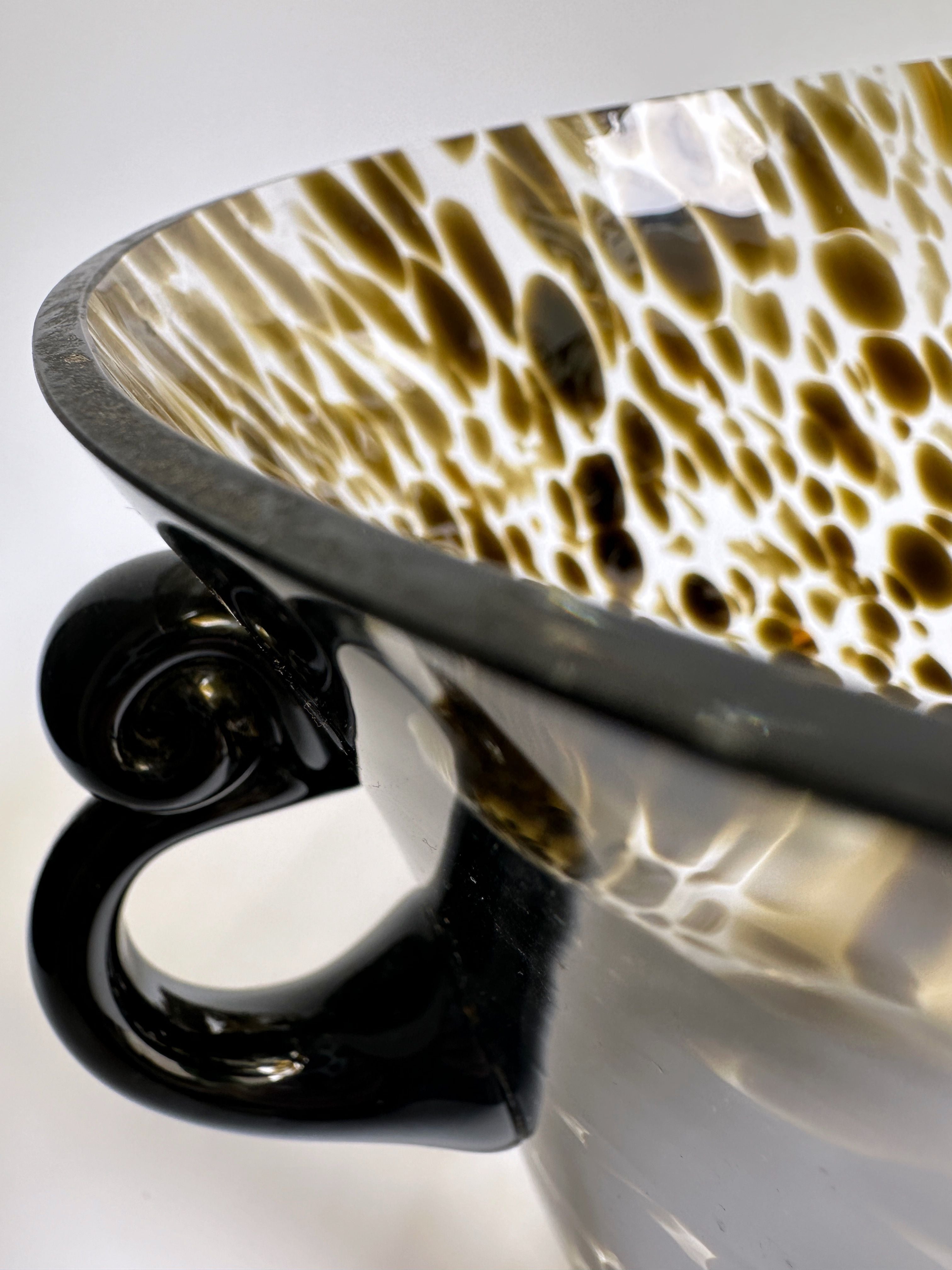 Close-up of the Dodo Vintage Art Deco Champagne Bucket featuring a gloss black exterior and a spotted brown and white interior pattern. The handle, with its smooth, shiny black finish, is visible on the left side. Reminiscent of tortoise glass vase aesthetics, the focus is on the intricate detail and texture of this exquisite design.