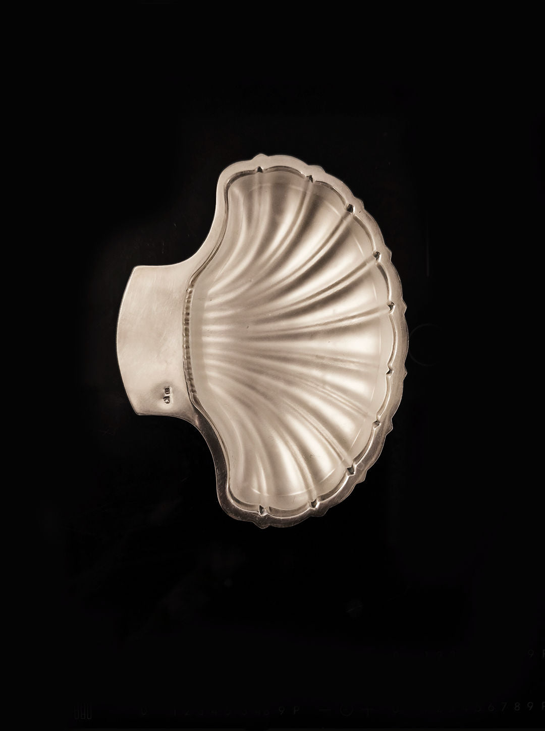 The Les Objoies Shell Butter Dish is a silver-plated, vintage-style serving piece designed as a scallop shell with detailed ridges, a polished finish, and a handle on one side. Displayed on black, it exudes timeless charm.