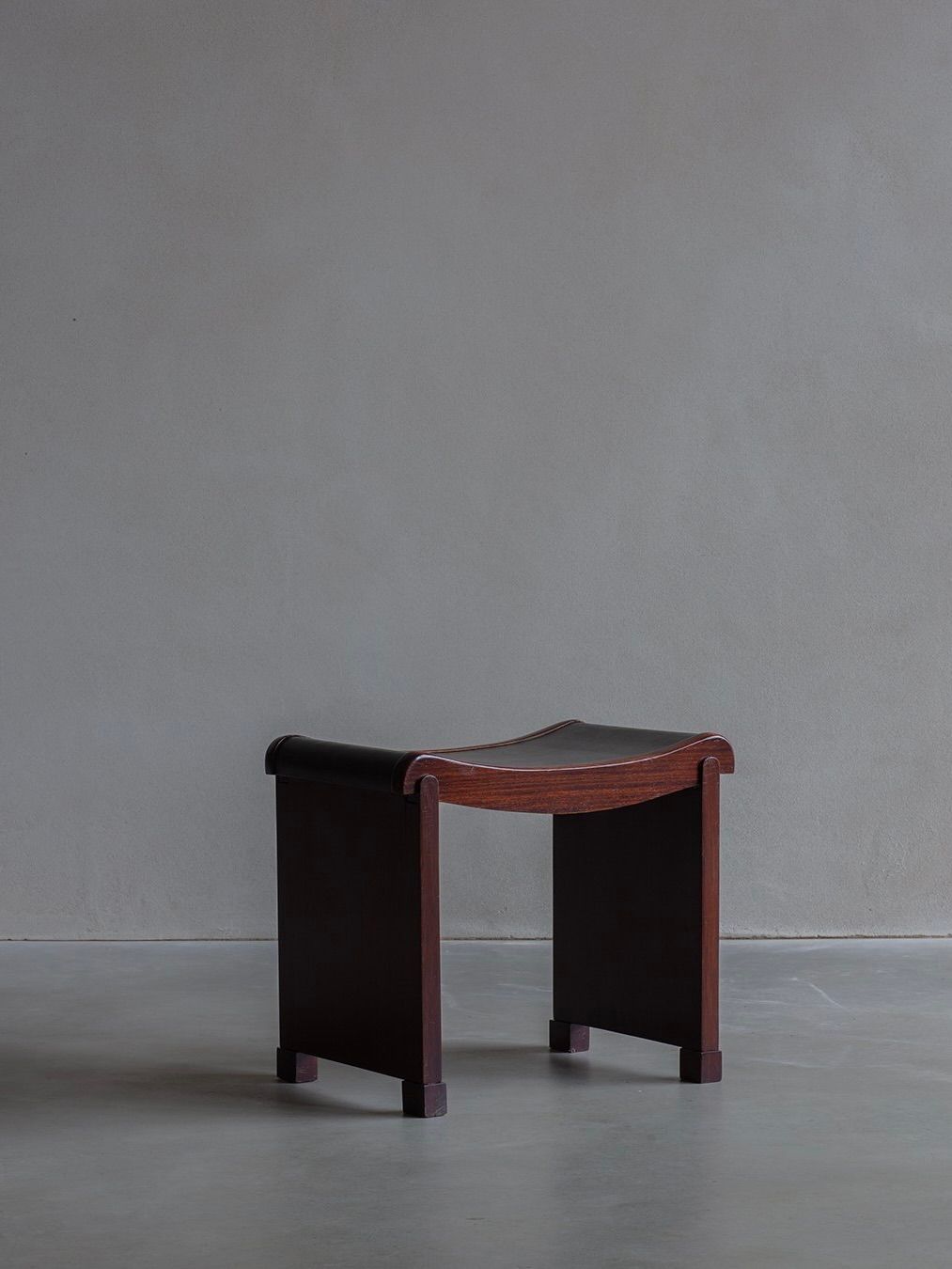 The Bicci de’ Medici Pierre Chareau - Curule Model No. MT 1015 Stool, inspired by Art Deco elements, features a minimalist dark wood finish with black accents on the legs and seat, set against a plain gray background.