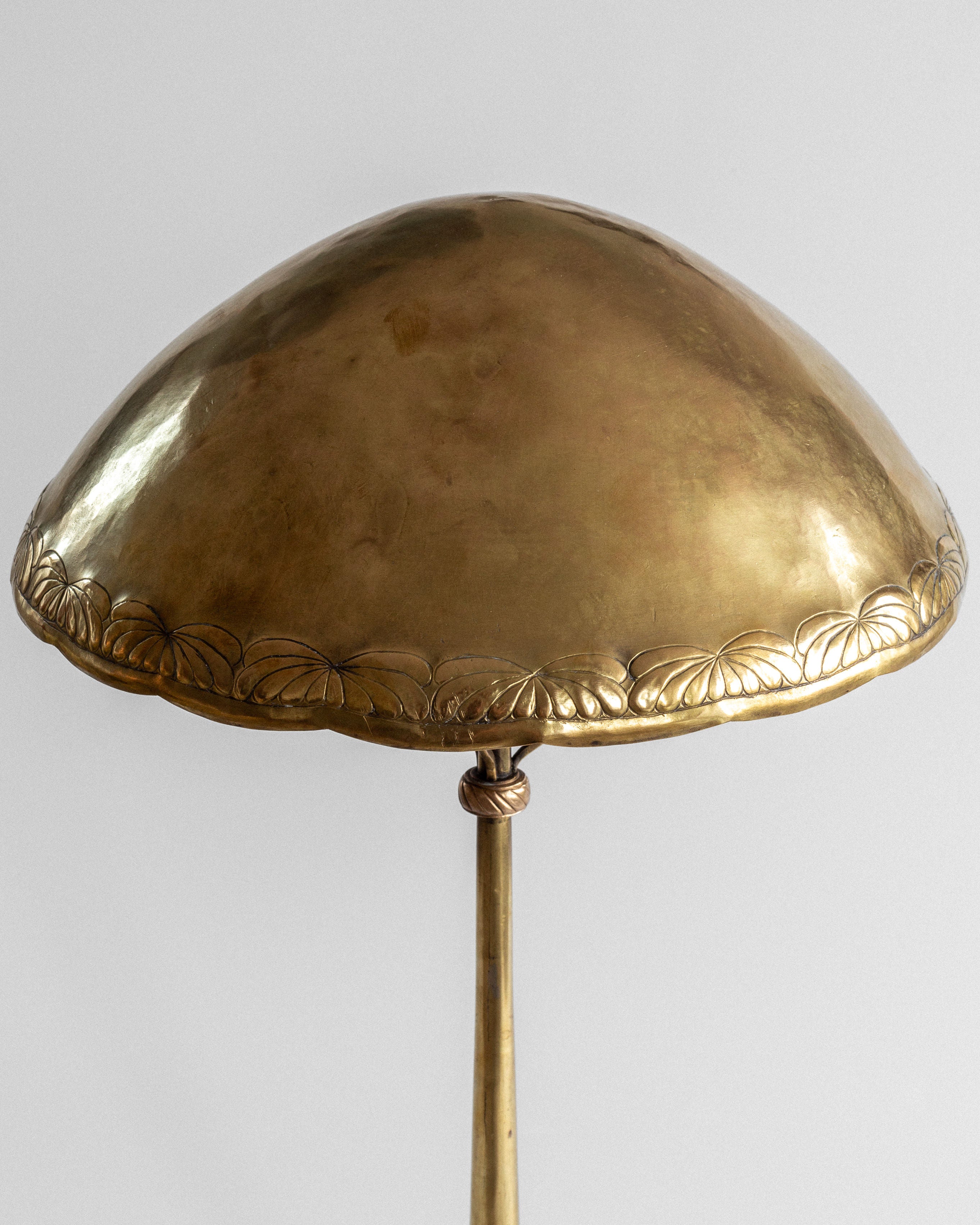 The Spigel Art Nouveau Brass Table Lamp stands elegantly on a slender pole with a dome-shaped shade featuring floral engravings against a plain background.