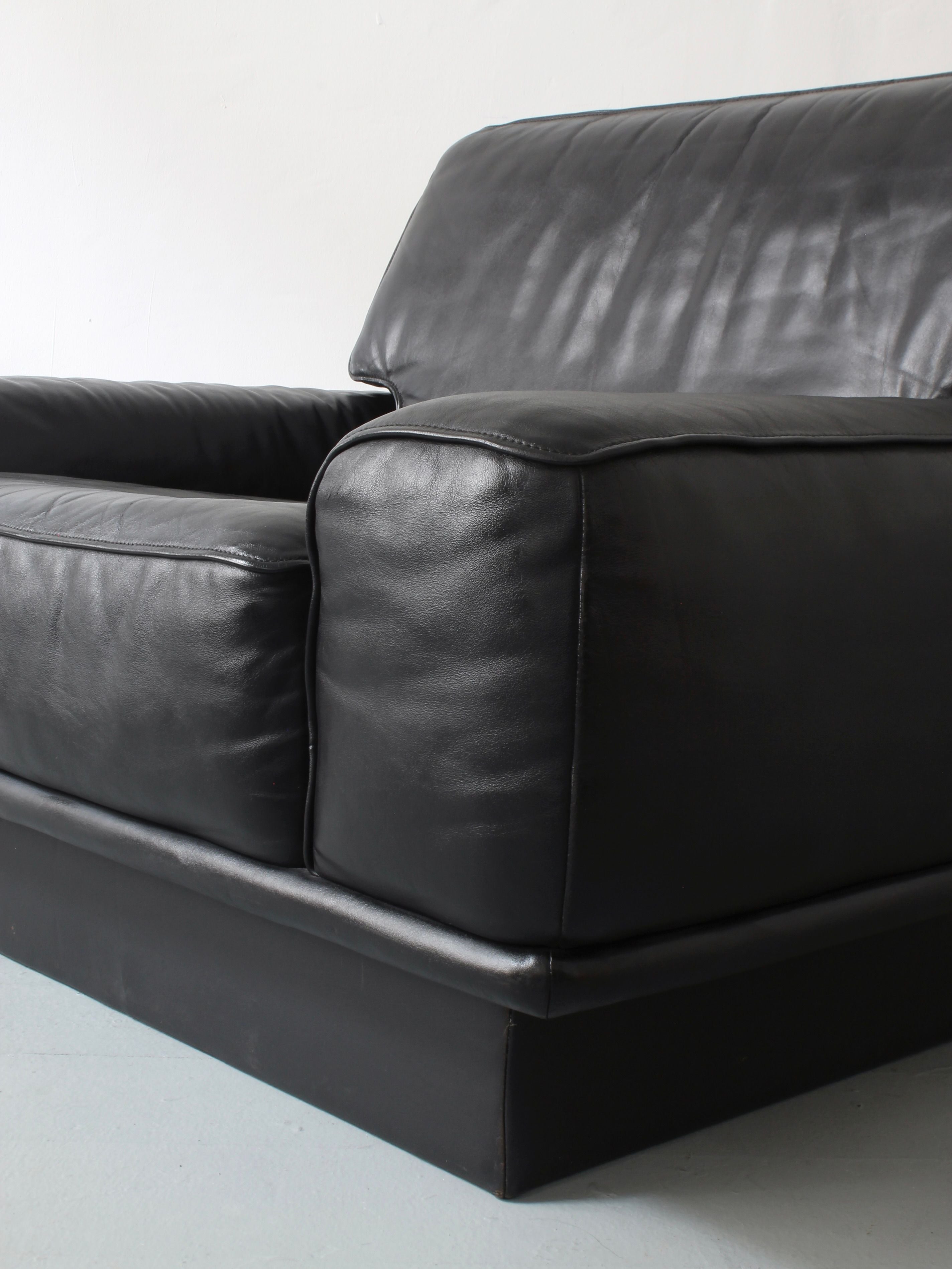 Close-up of a Lounge Chair by De Sede from Afterhour Furniture, focusing on the black, smooth-finish leather armrest and seat cushion. This piece exemplifies Swiss luxury with its visible creases, set against a plain white background.