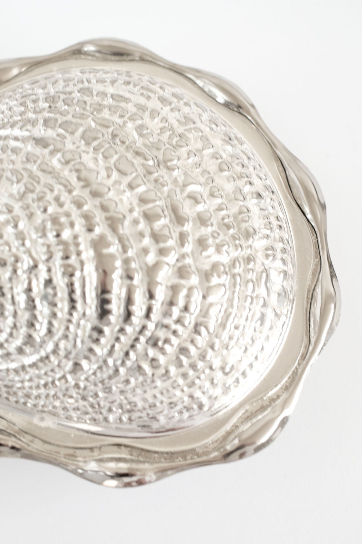 Close-up of the septembre studios Shell Butter Dish—a shiny, textured silver piece resembling a vintage scallop shell with a wavy edge, set against a white background.