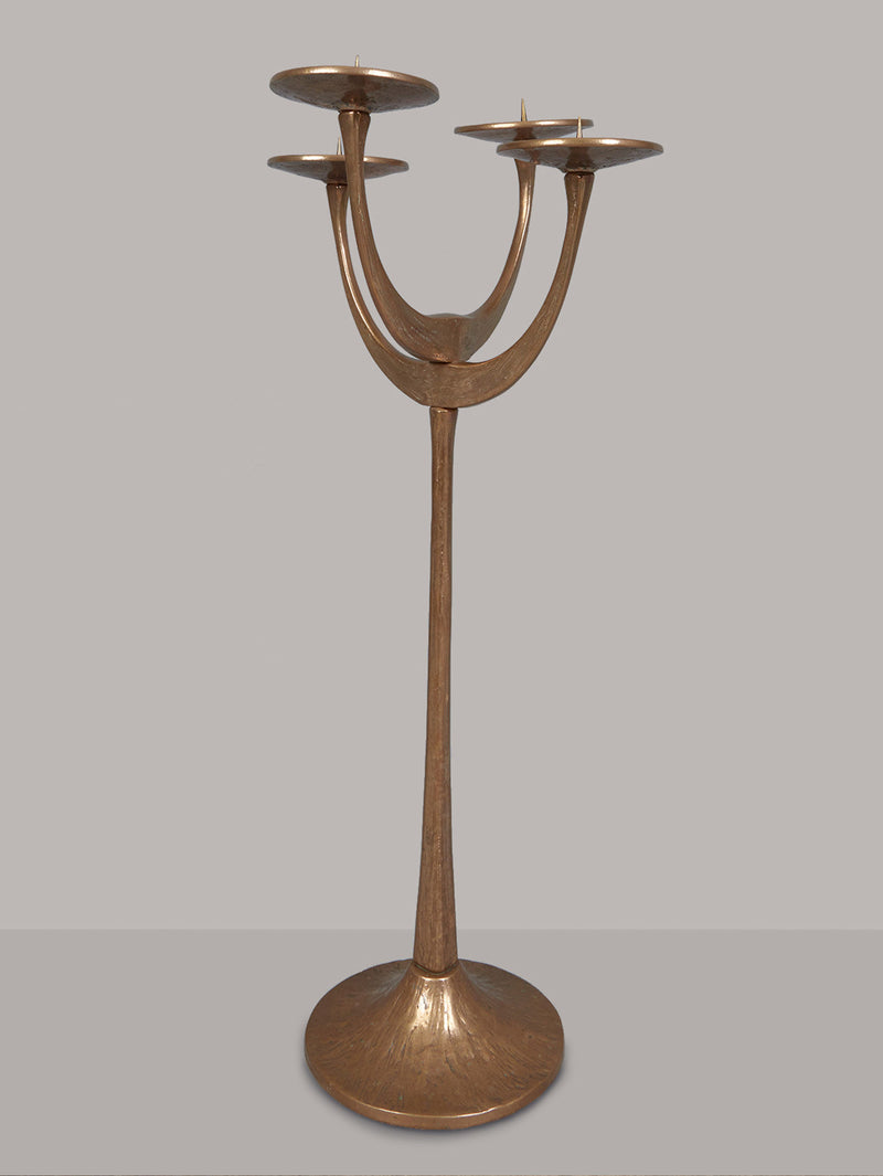 The Floor Standing Brutalist Candleholder by Tobias Harjes for RELIC LONDON features three curved arms from a central stem, each with a circular holder. Made of bell bronze, its modern design includes an elegant bronze-like finish and a wide round base for stability.
