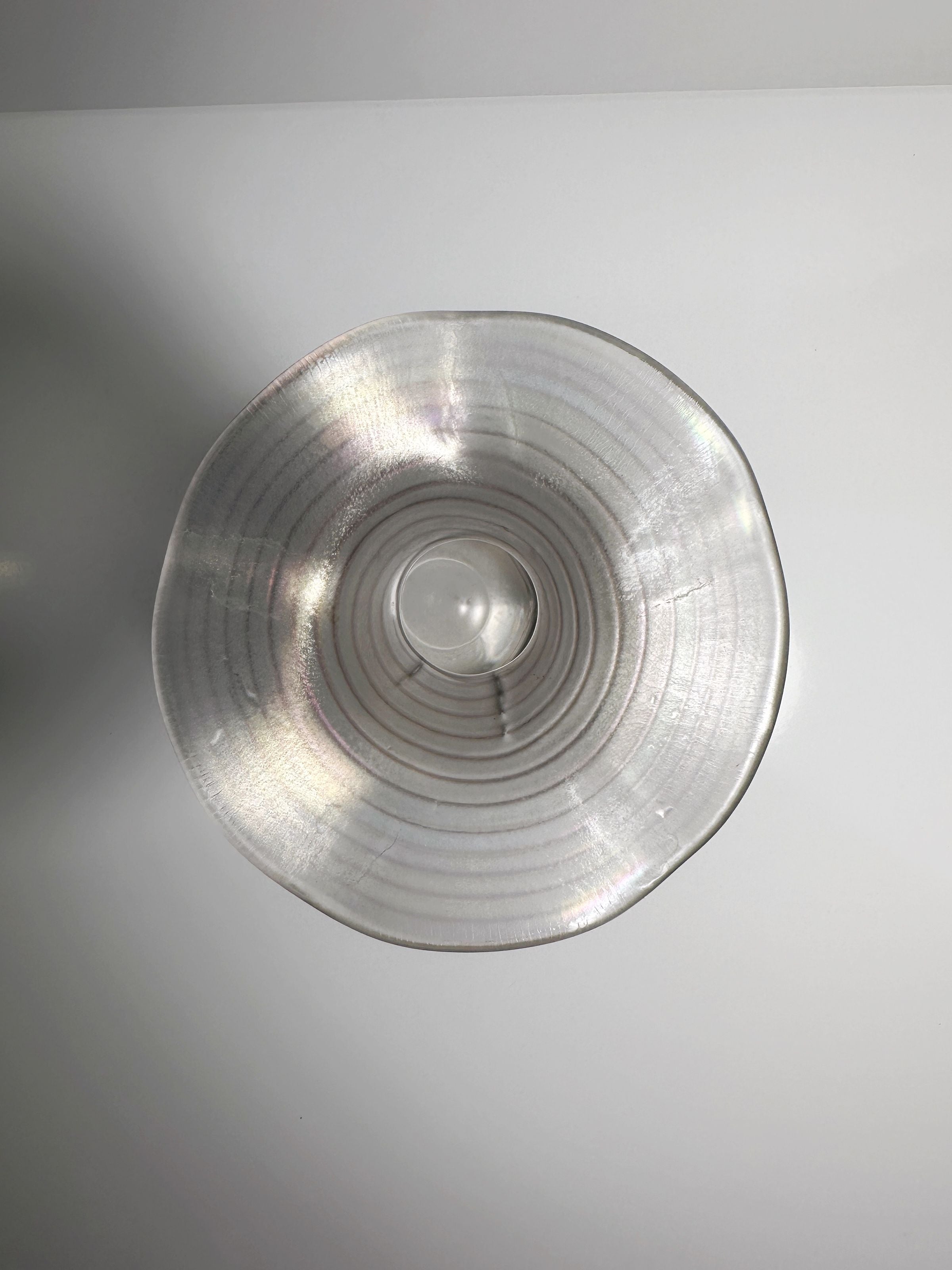 Top view of a Dodo Vintage-design, translucent circular glass bowl with concentric rings against a white background. The bowl's surface reflects light, creating an iridescent effect reminiscent of the Art Nouveau Wavy Vase.