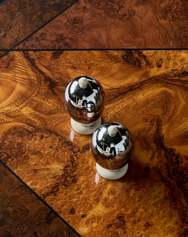 Two chrome and marble egg warmers on burl wood table detail