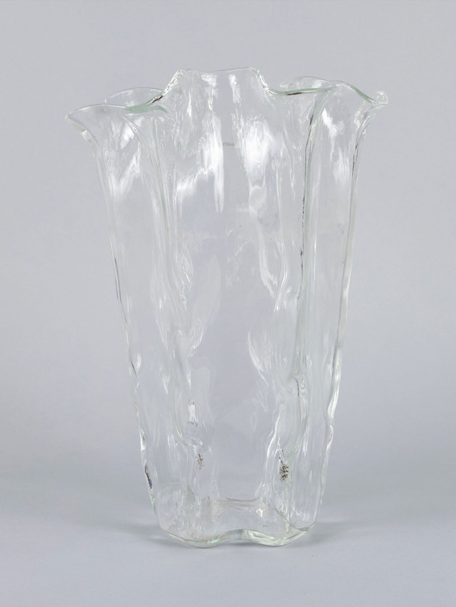 The Organic Glass Vase by Pertti Kallioinen for RELIC LONDON offers a wavy, organic design with a rippled texture like flowing water. It has a wide opening, translucent appearance, and is set against a gray background.