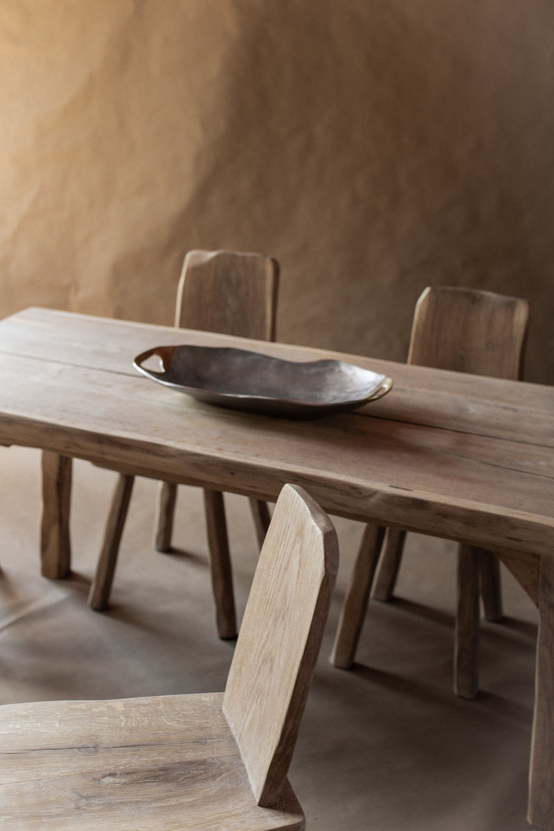 Dark ceramic brutalist bowl on natural wood dining table with chairs