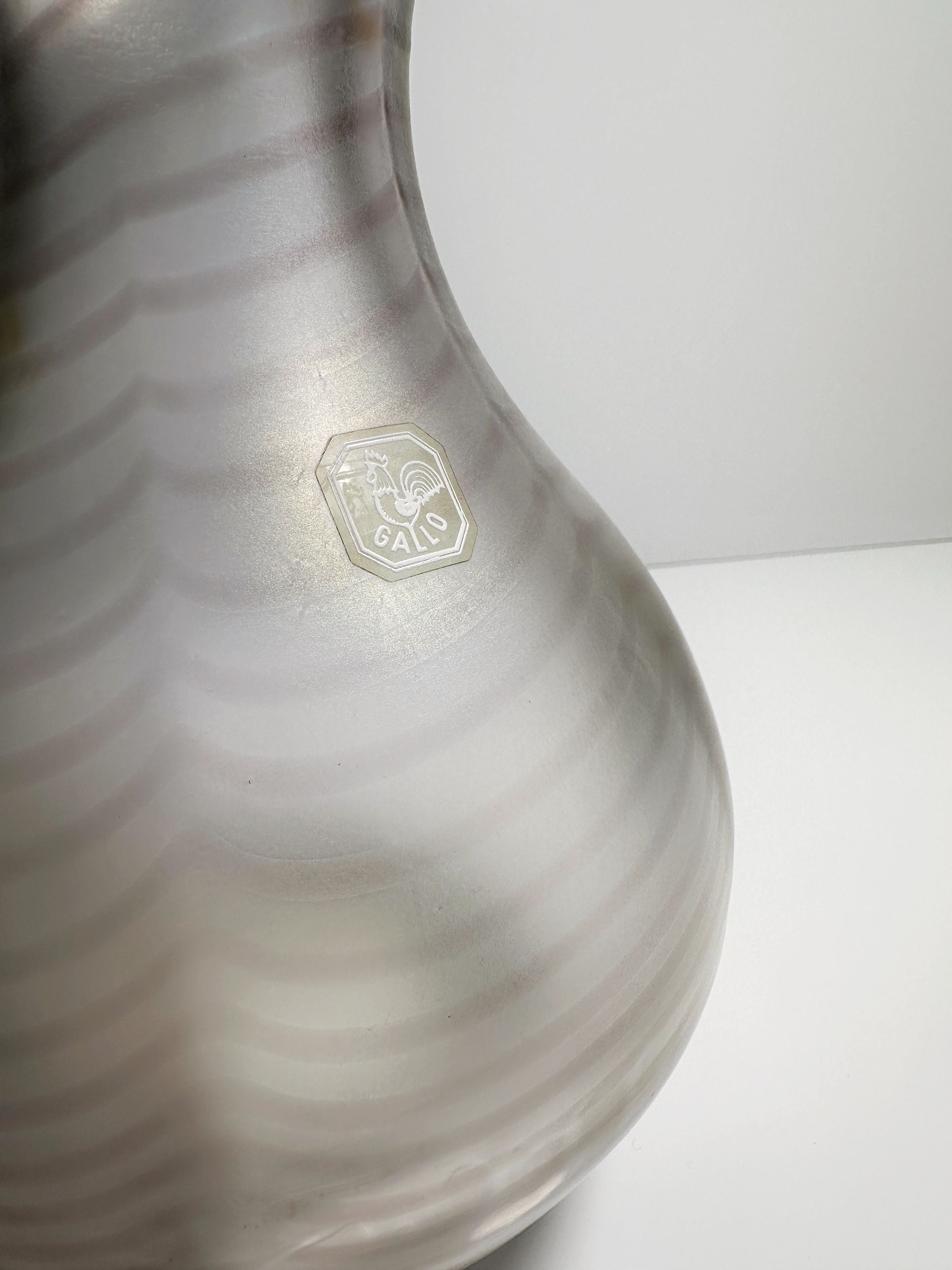 Close-up of the Art Nouveau Wavy Vase by Dodo Vintage, showcasing a light gray design with subtle horizontal stripes. The faintly iridescent surface enhances its charm, complemented by a small hexagonal emblem bearing the text "GALLO" and a rooster motif on the side.