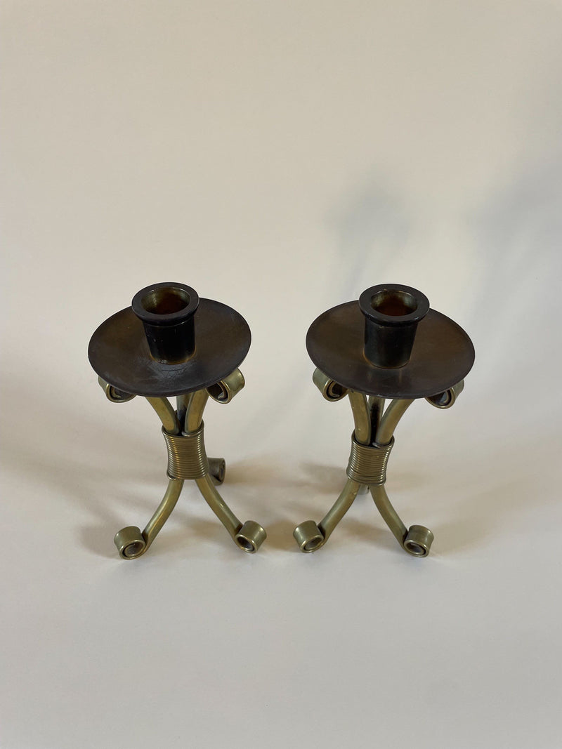 Two ornate Maud Vaughan Pair of Mid-Century Danish Candleholders with a sculptural form, featuring three elegantly curved legs and a slender central column, each topped with a wide plate and holder for a single candle. The background is a plain, off-white surface. These pieces embody mid-century elegance.