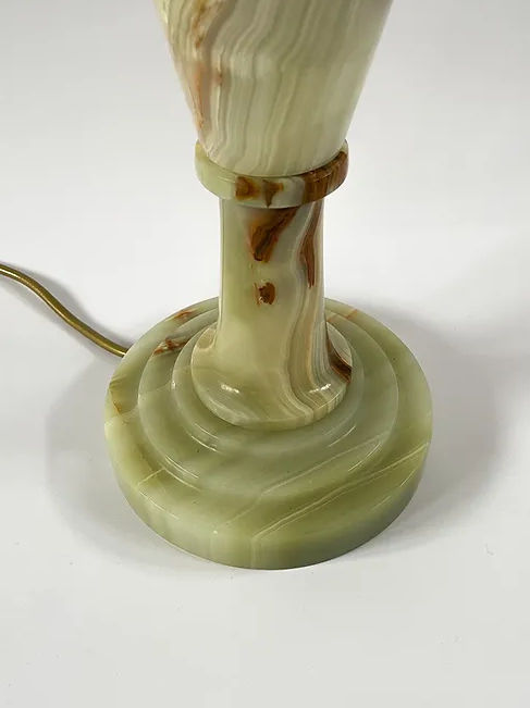 Close-up image of the base of a Large Vintage Onyx Lamp by Maud Vaughan, showcasing its green hues and brown veining. The lamp base features a round bottom with a slender, tapering column above it. An antique gold flex power cord is attached to the base and extends out of the frame.