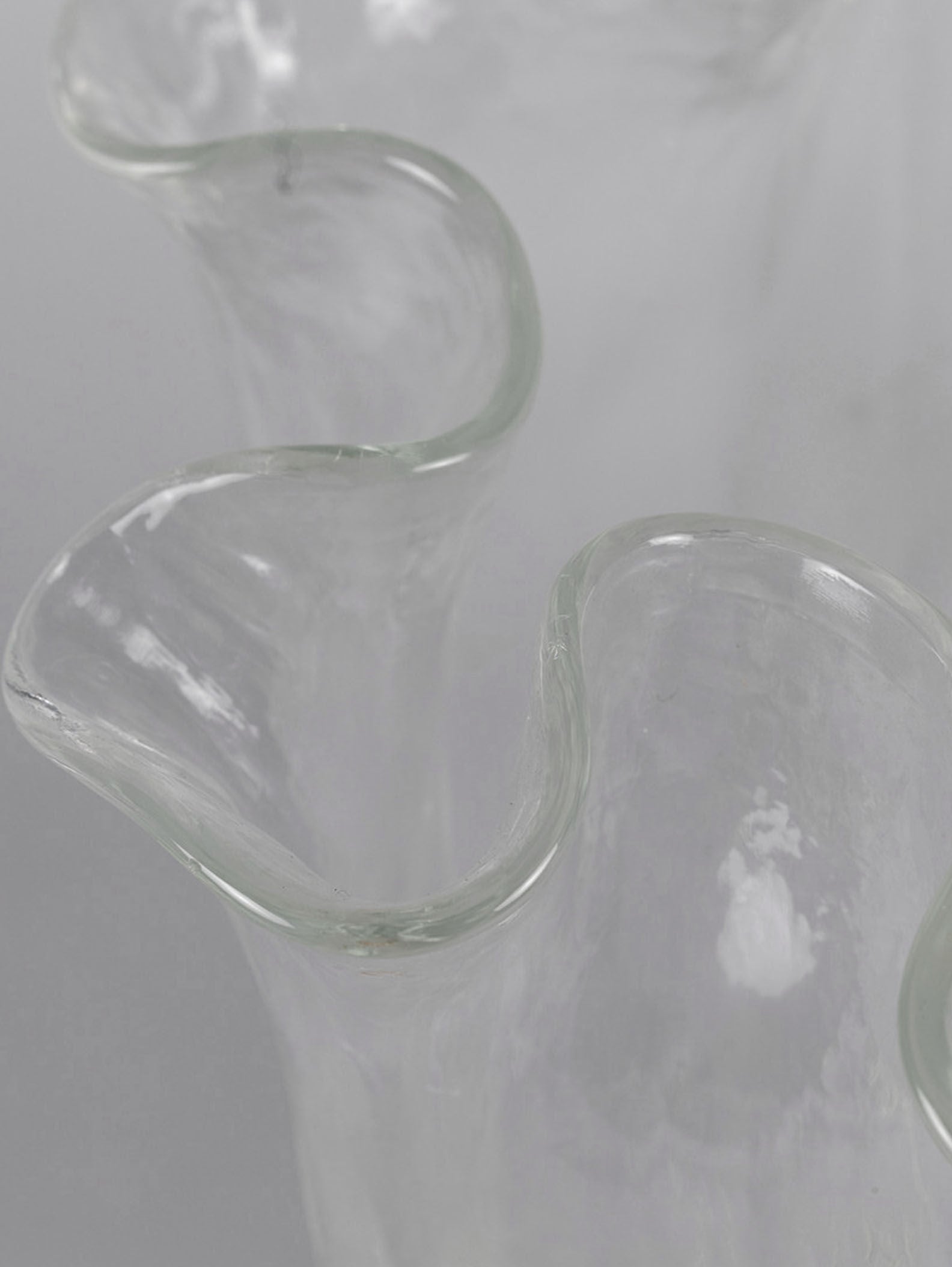 Close-up of a clear, wavy-edged Glass Vase by Pertti Kallioinen from RELIC LONDON, set against a soft grey background. The delicate, undulating rim adds an artistic, flowing appearance to this exquisite design.